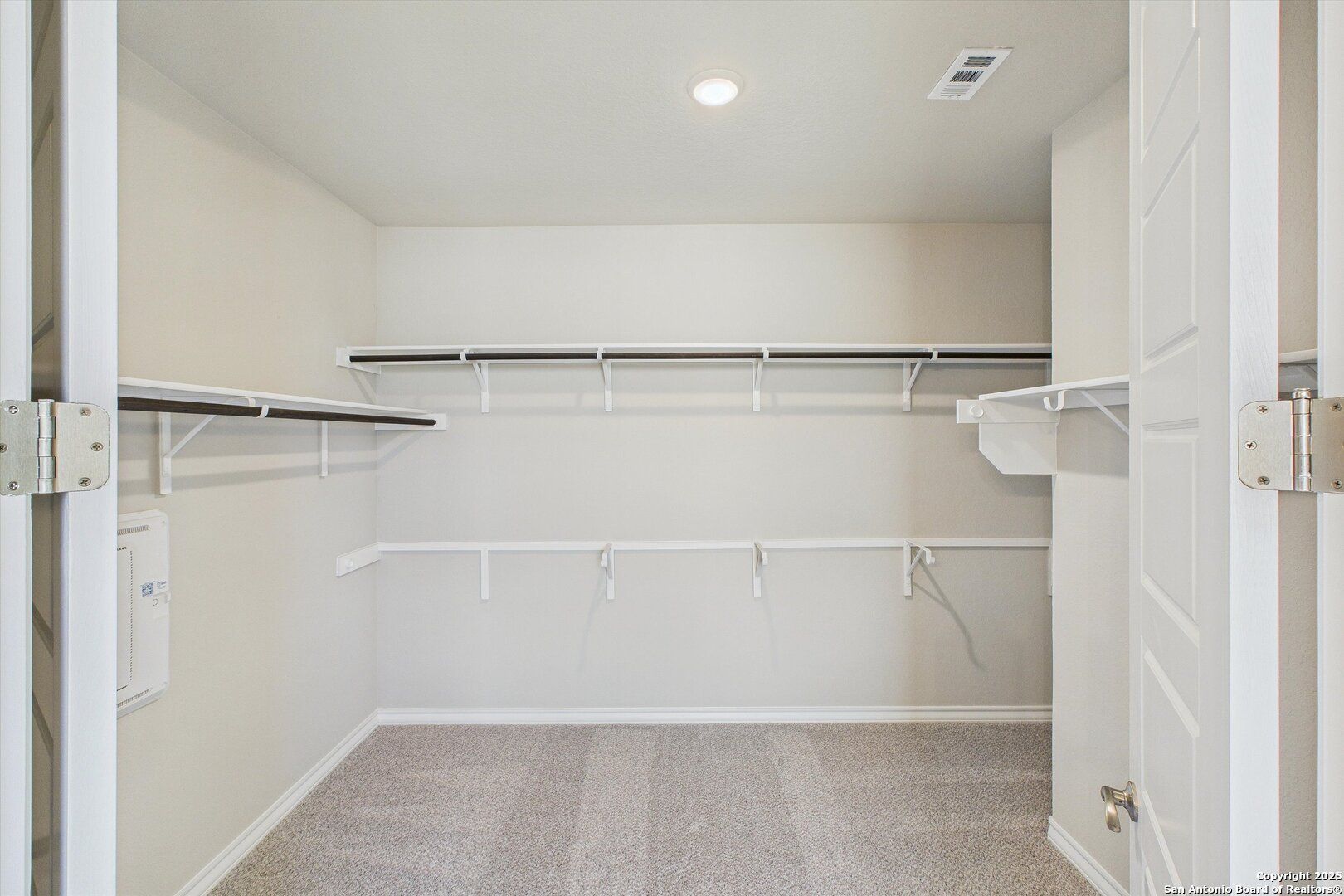 Spacious walk-in closet with white shelving and hanging rods in master suite of 5-bedroom Davidson Homes The Jennings H, Ladera, San Antonio