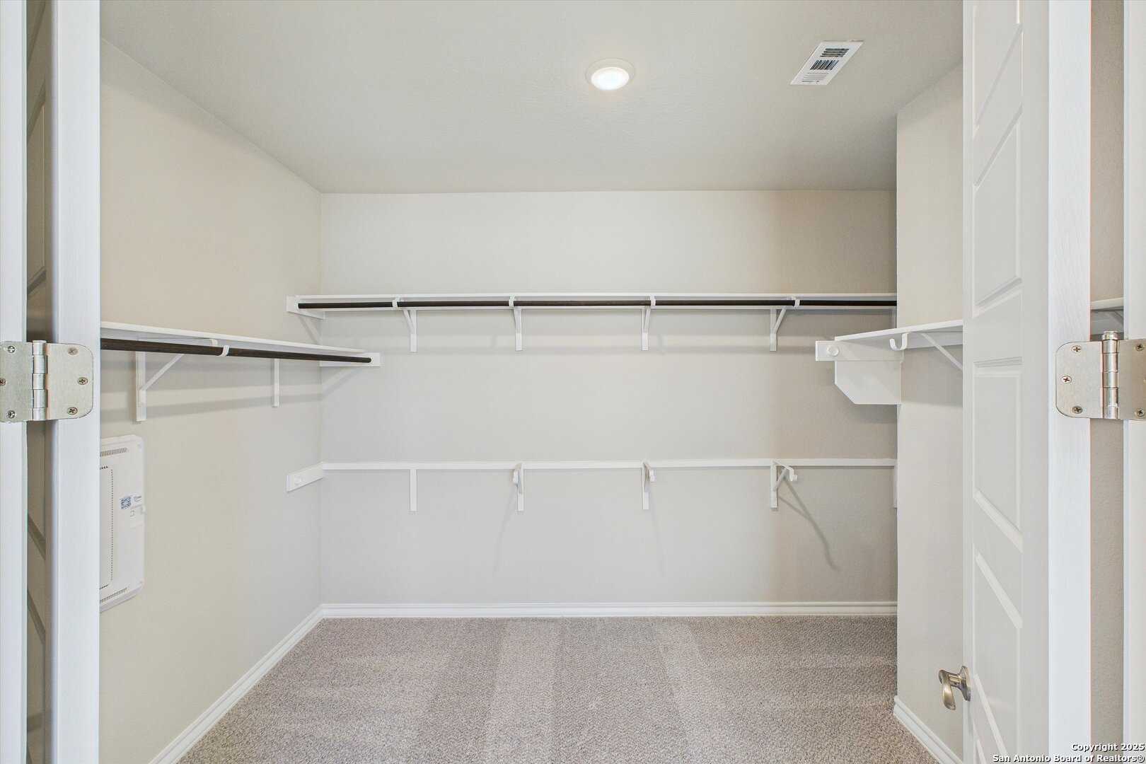 Spacious walk-in closet with white shelving and hanging rods in master suite of 5-bedroom Davidson Homes The Jennings H, Ladera, San Antonio