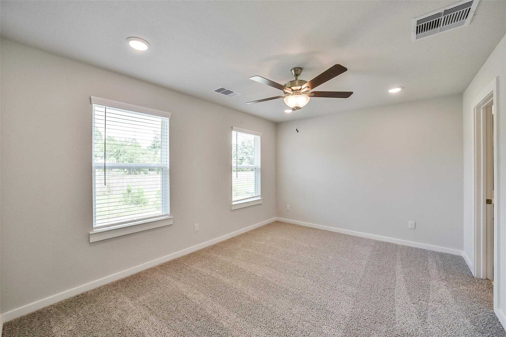 Bright secondary bedroom with beige carpet, ceiling fan, large windows, and neutral walls in Davidson Homes The Trinity F, Magnolia, Texas