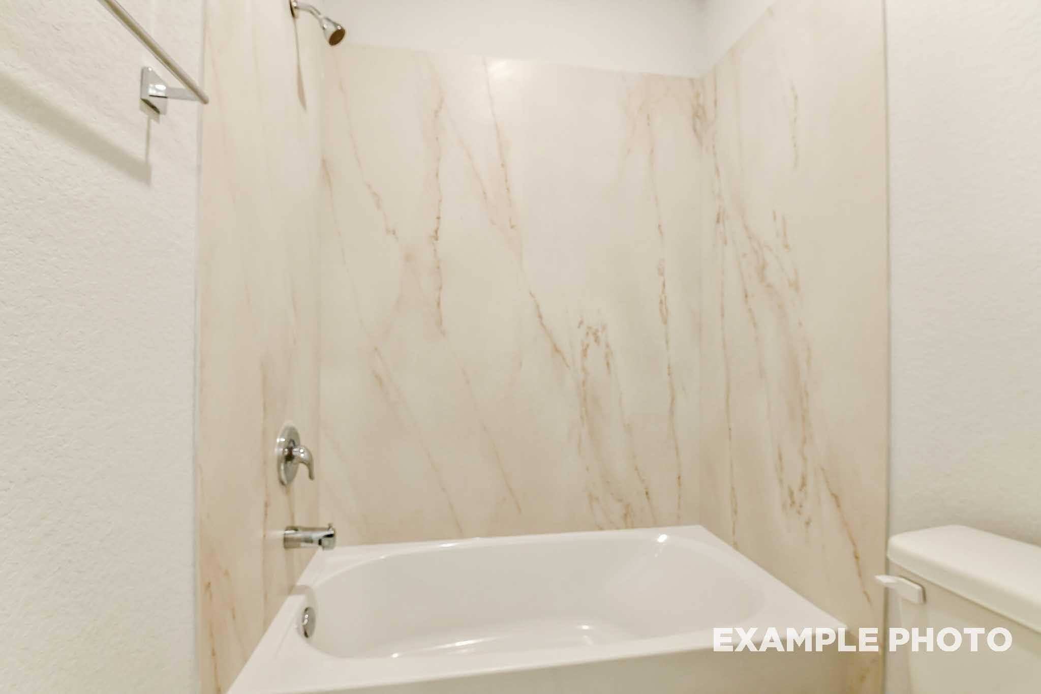 Elegant bathroom with marble-look tiled walls, white soaking tub, glass shower, and modern fixtures in Davidson Homes The Colorado G, Conroe Texas