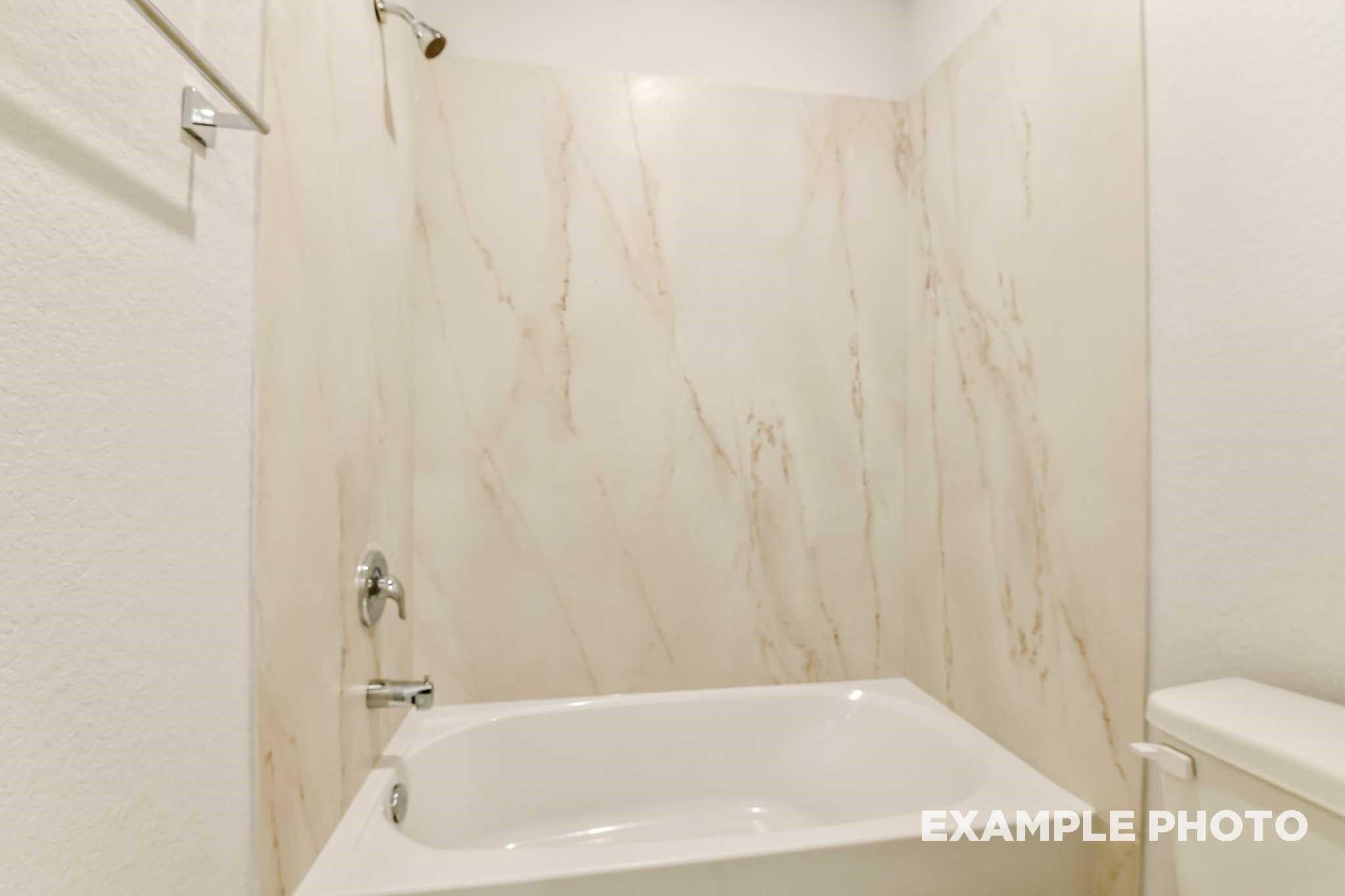 Elegant bathroom with marble-look tiled walls, white soaking tub, glass shower, and modern fixtures in Davidson Homes The Colorado G, Conroe Texas