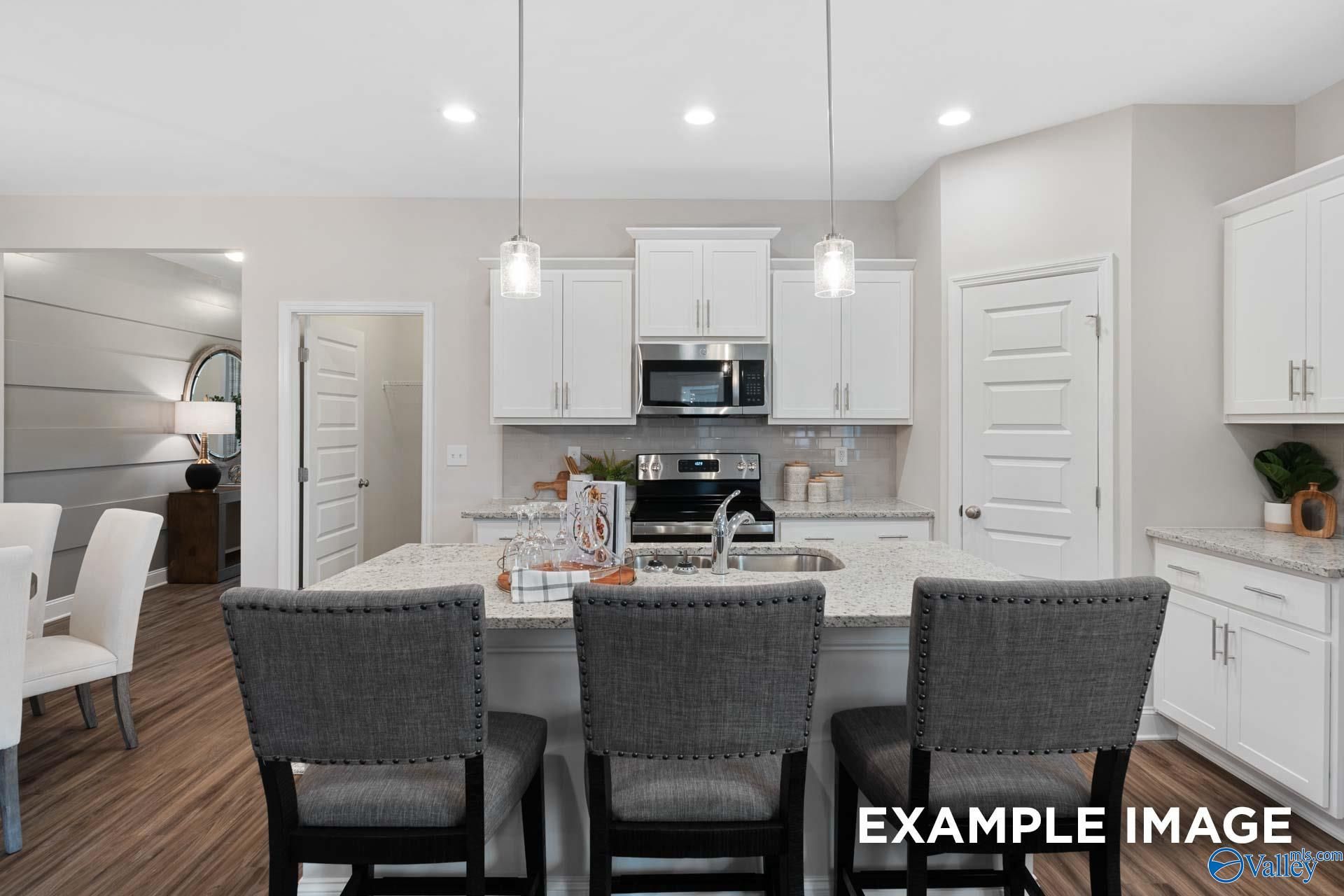 Kitchen island with granite countertops, white cabinetry, and pendant lighting in Davidson Homes The Camilla C, Hartselle, Alabama