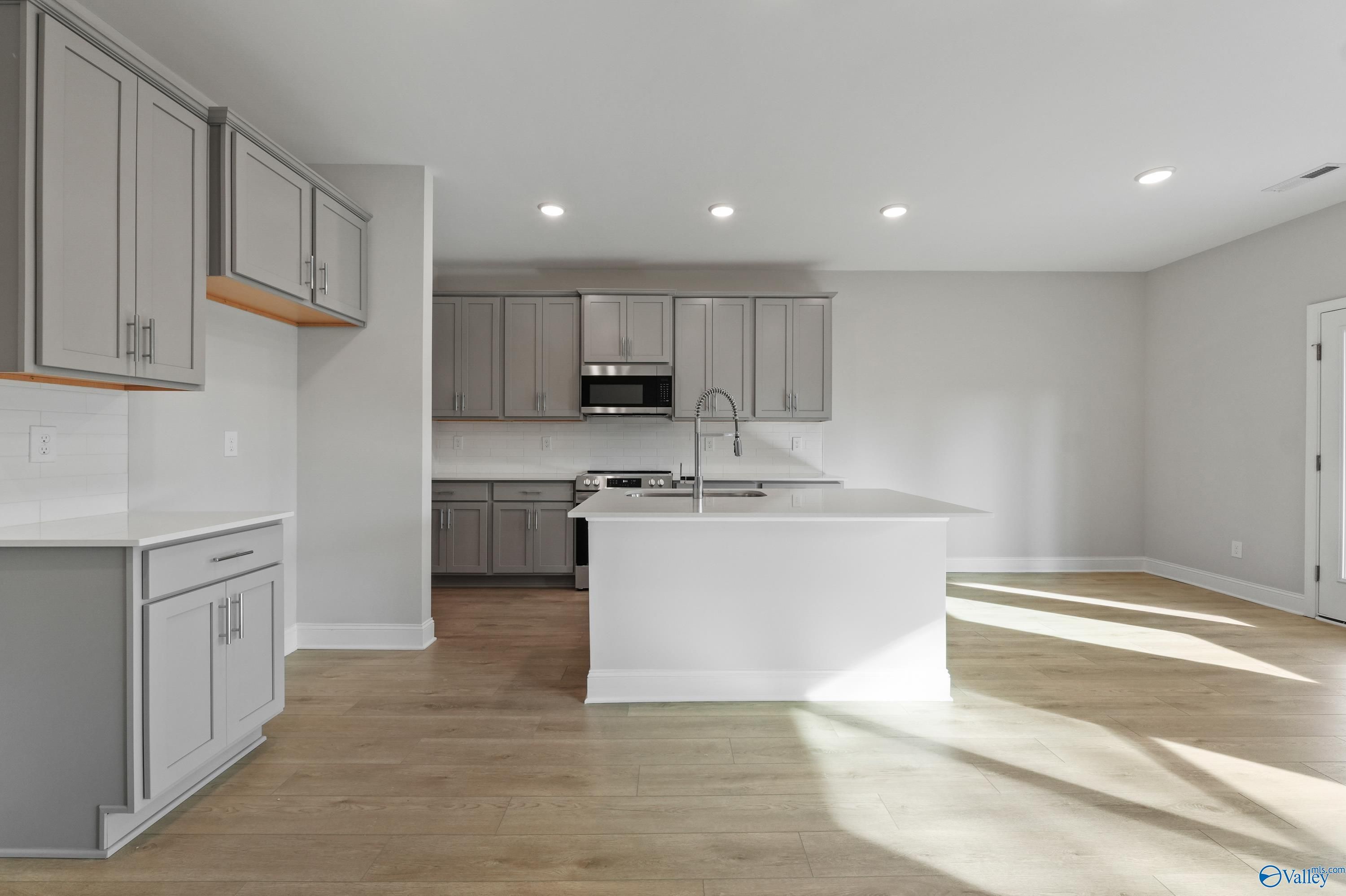 Modern gray shaker cabinets, white quartz island, stainless sink and appliances in The Camden B kitchen, Huntsville AL