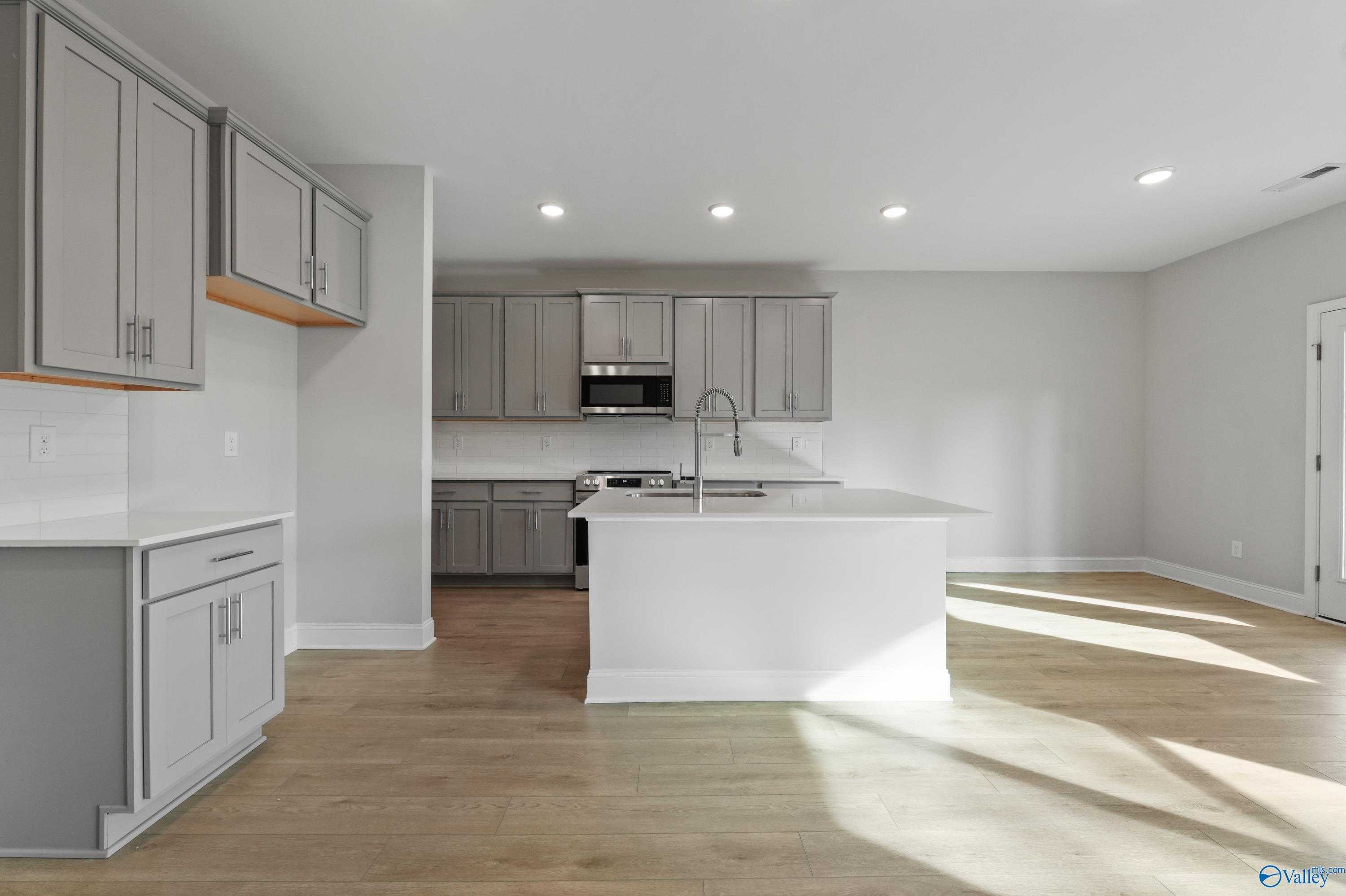 Modern gray shaker cabinets, white quartz island, stainless sink and appliances in The Camden B kitchen, Huntsville AL