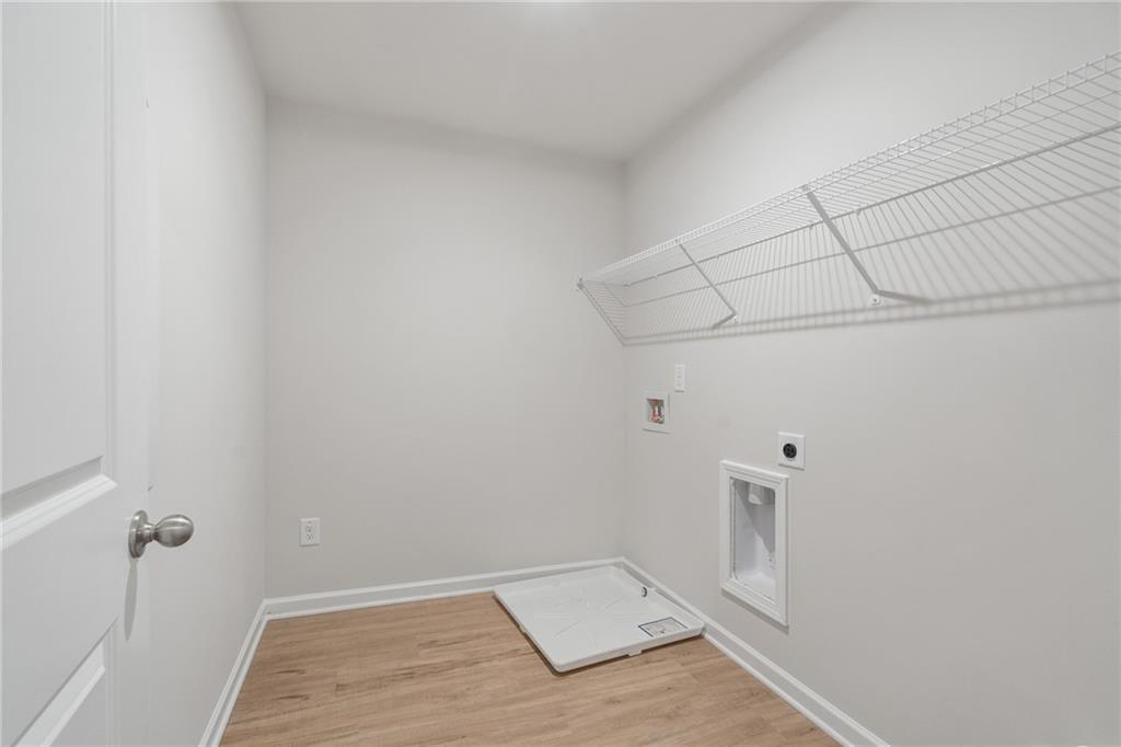 Spacious laundry room with wire shelving, utility sink, and hardwood floors in Davidson Homes The Cary A, Kennesaw, Georgia