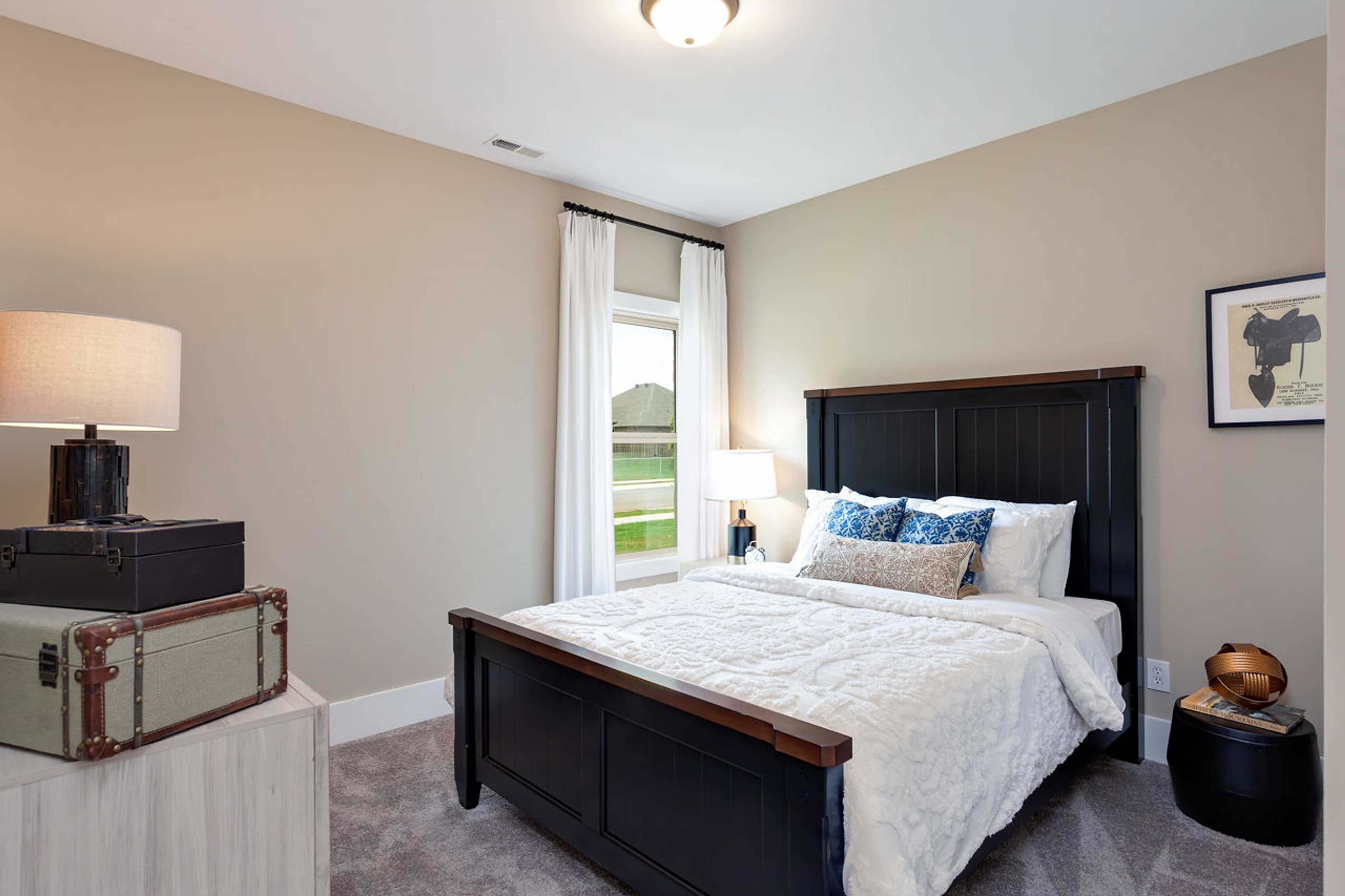 Cozy bedroom with black wooden queen bed, white bedding, blue pillows, beige walls, and garden view window at Williams Pointe in Huntsville Alabama