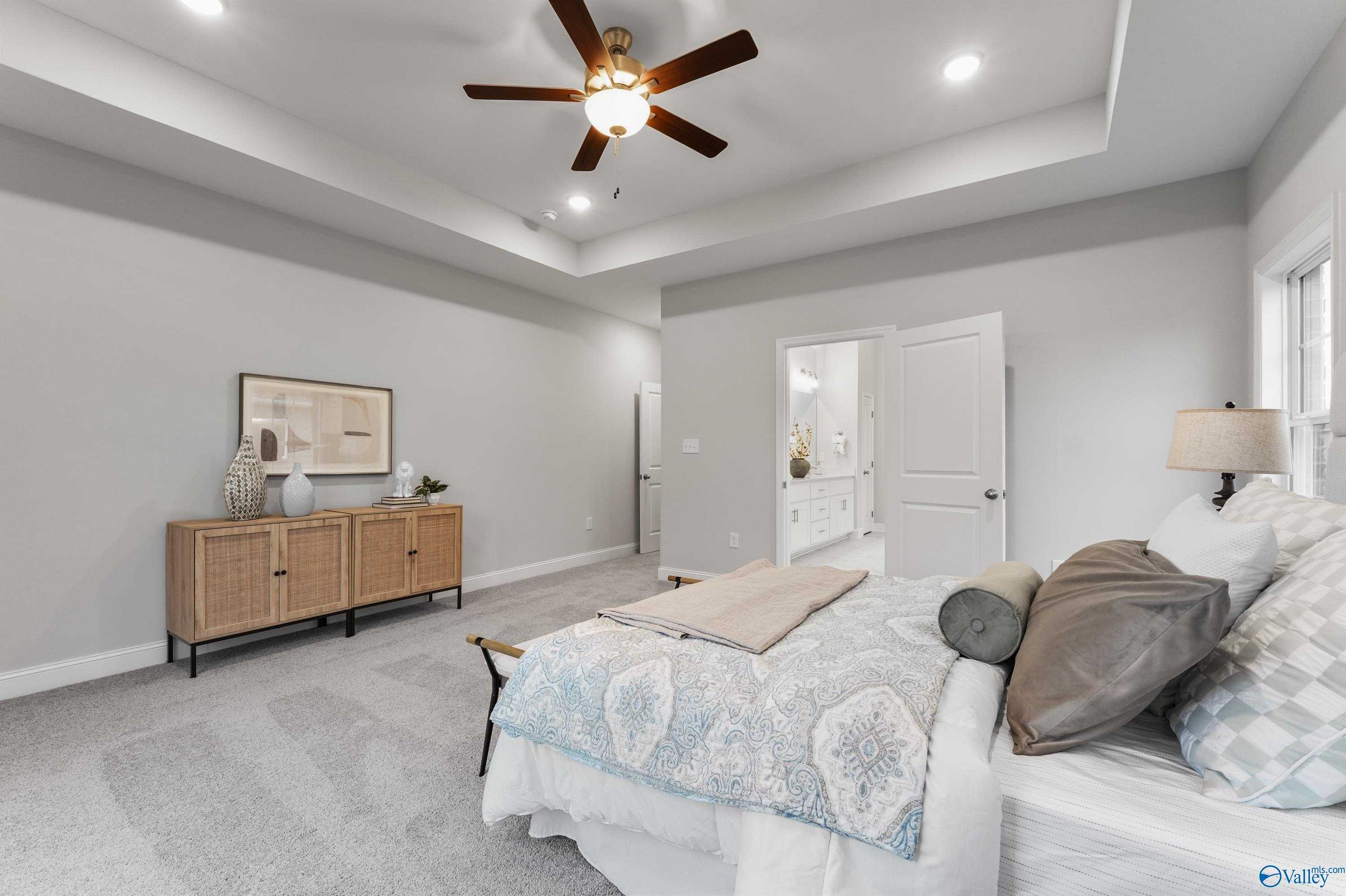 Spacious master bedroom with ceiling fan, plush king bed, rattan dresser in Davidson Homes The Finleigh, Toney, Alabama
