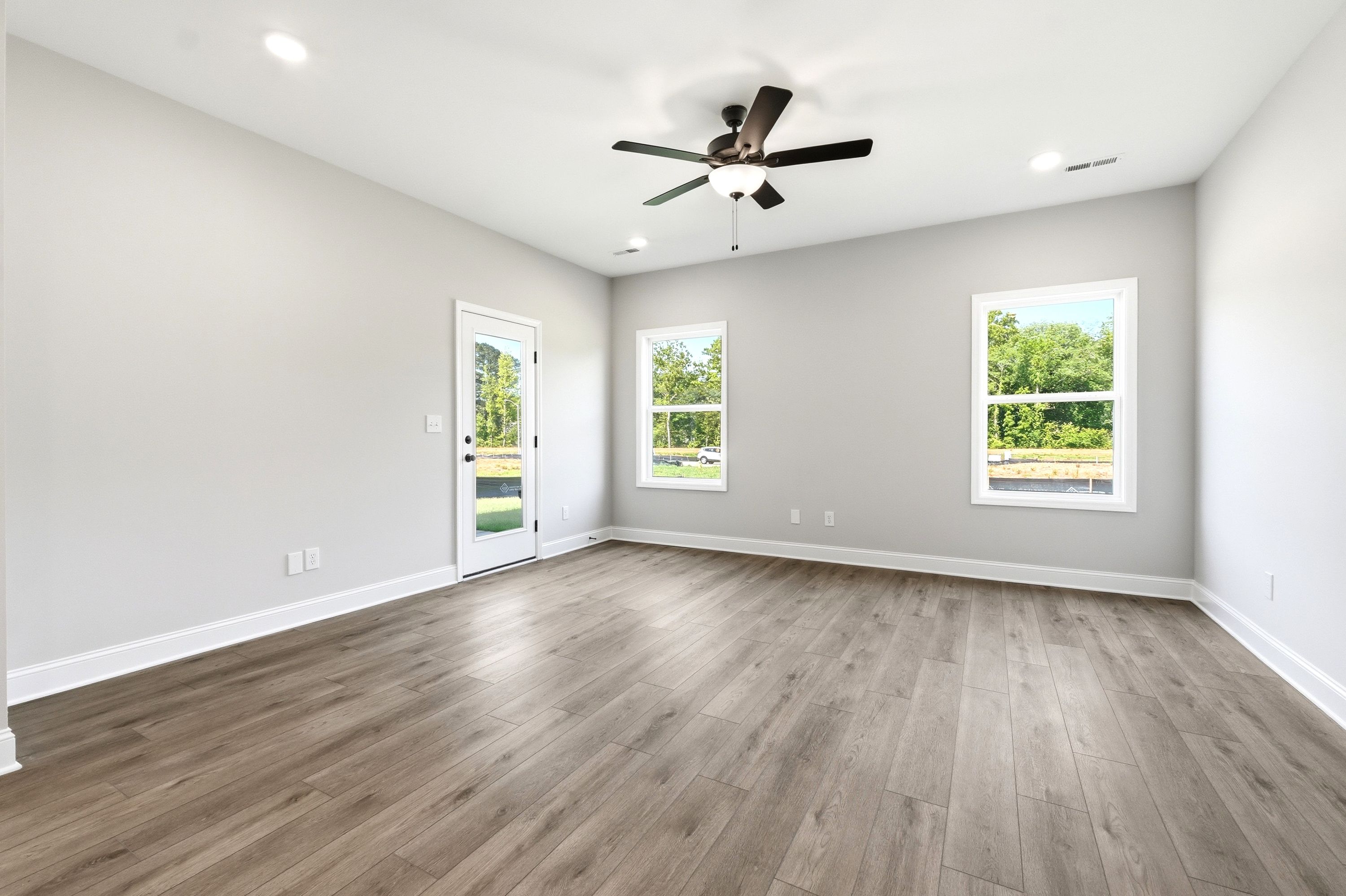 Spacious living area in The Russell A floor plan featuring wood-style flooring, a ceiling fan, and backyard access.