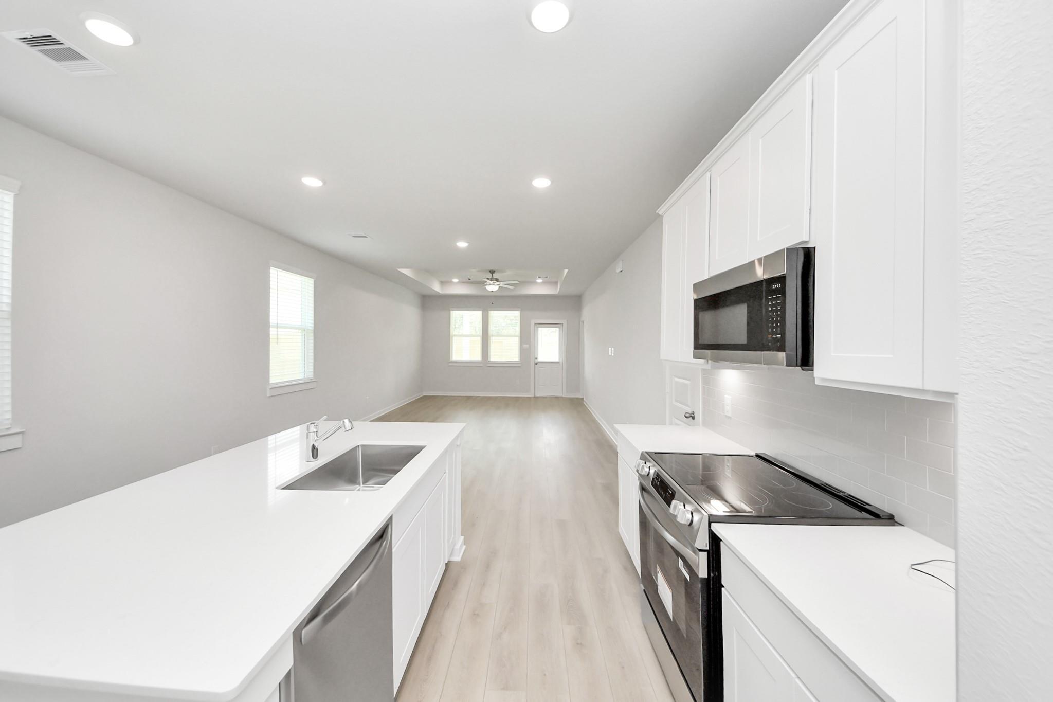 Modern white kitchen with island and stainless appliances in The Frio F floor plan at Liberty Estates, Cleveland, Texas.