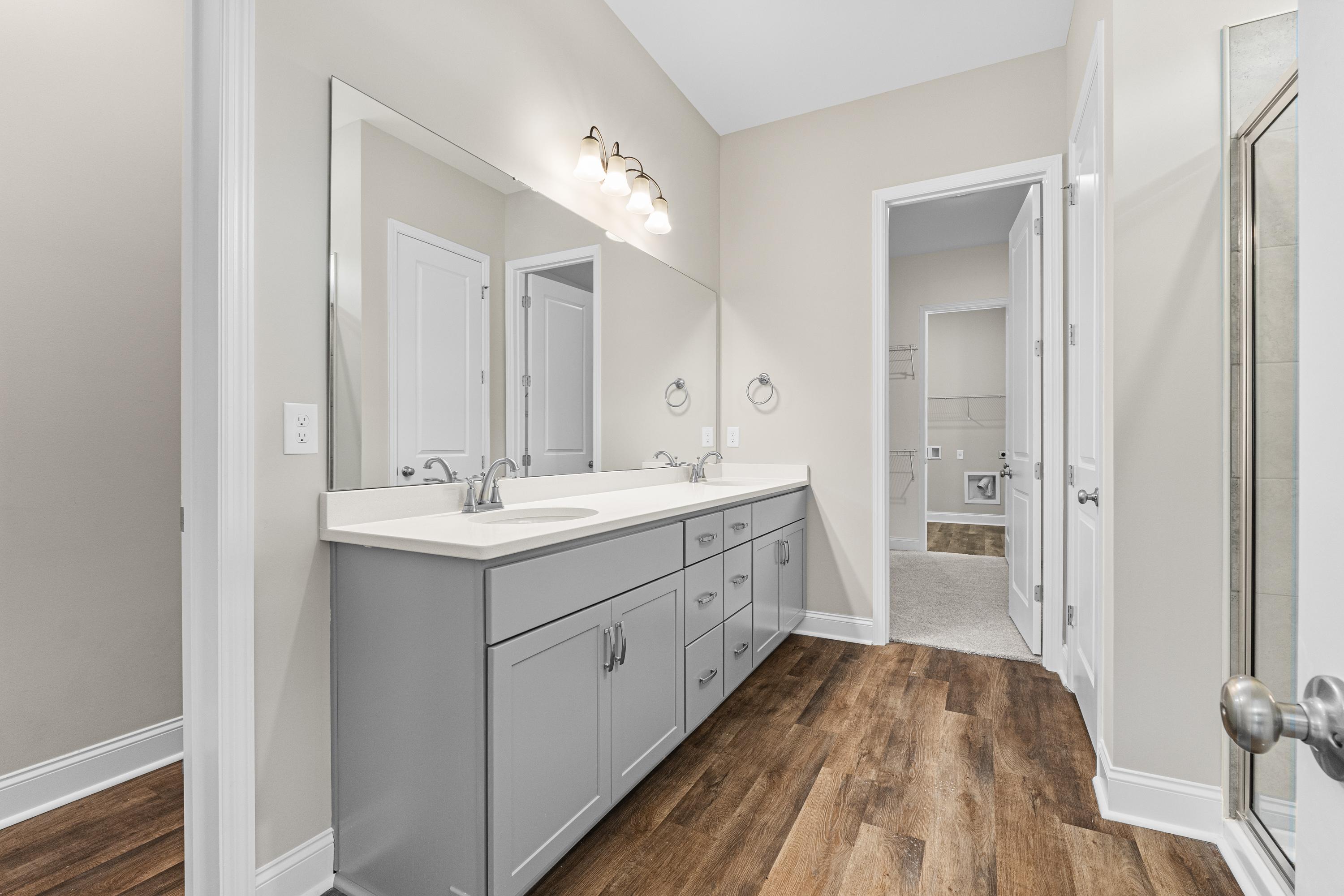 Spacious master bathroom in The Arcadia B featuring gray double vanity, large mirror, and wood-look flooring
