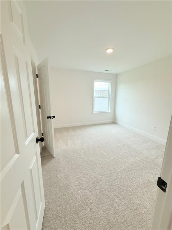 Spacious secondary bedroom with neutral carpet and white walls in The Hickory B floor plan at Wehunt Meadows, Hoschton.