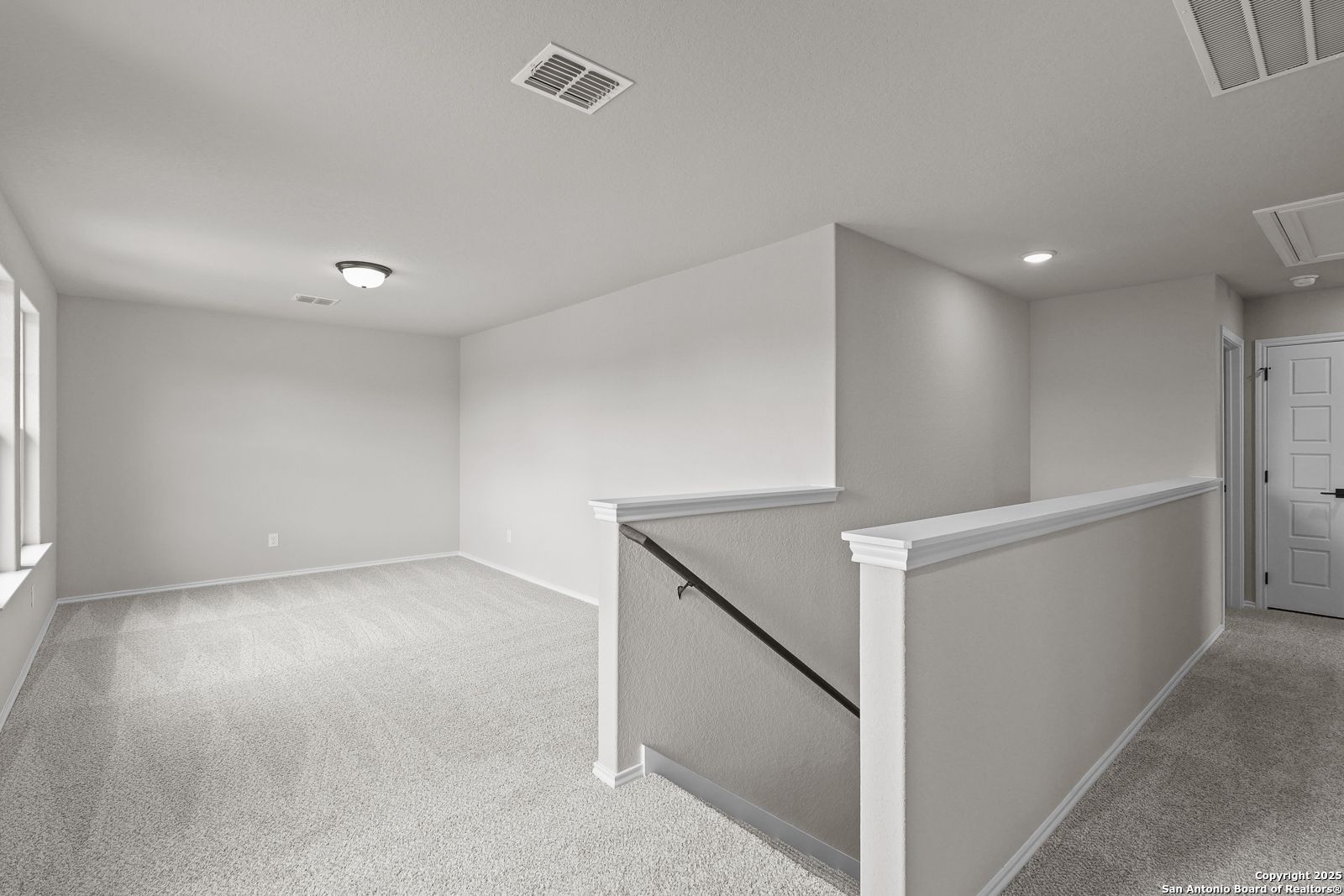 Bright upstairs loft with beige walls, carpeted floors, staircase railing, and large windows in Davidson Homes The Murray J, San Antonio