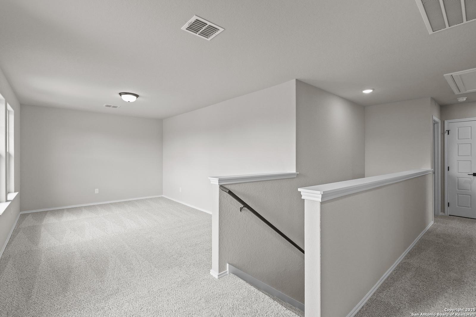 Bright upstairs loft with beige walls, carpeted floors, staircase railing, and large windows in Davidson Homes The Murray J, San Antonio
