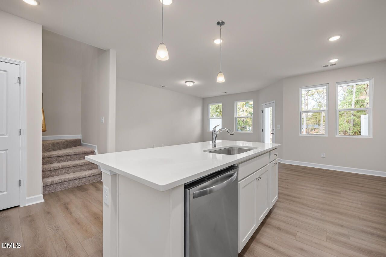 Modern open kitchen with white island, stainless dishwasher, sink, hardwood floors, and pendant lights in Davidson Homes The Graham, Fuquay-Varina, NC