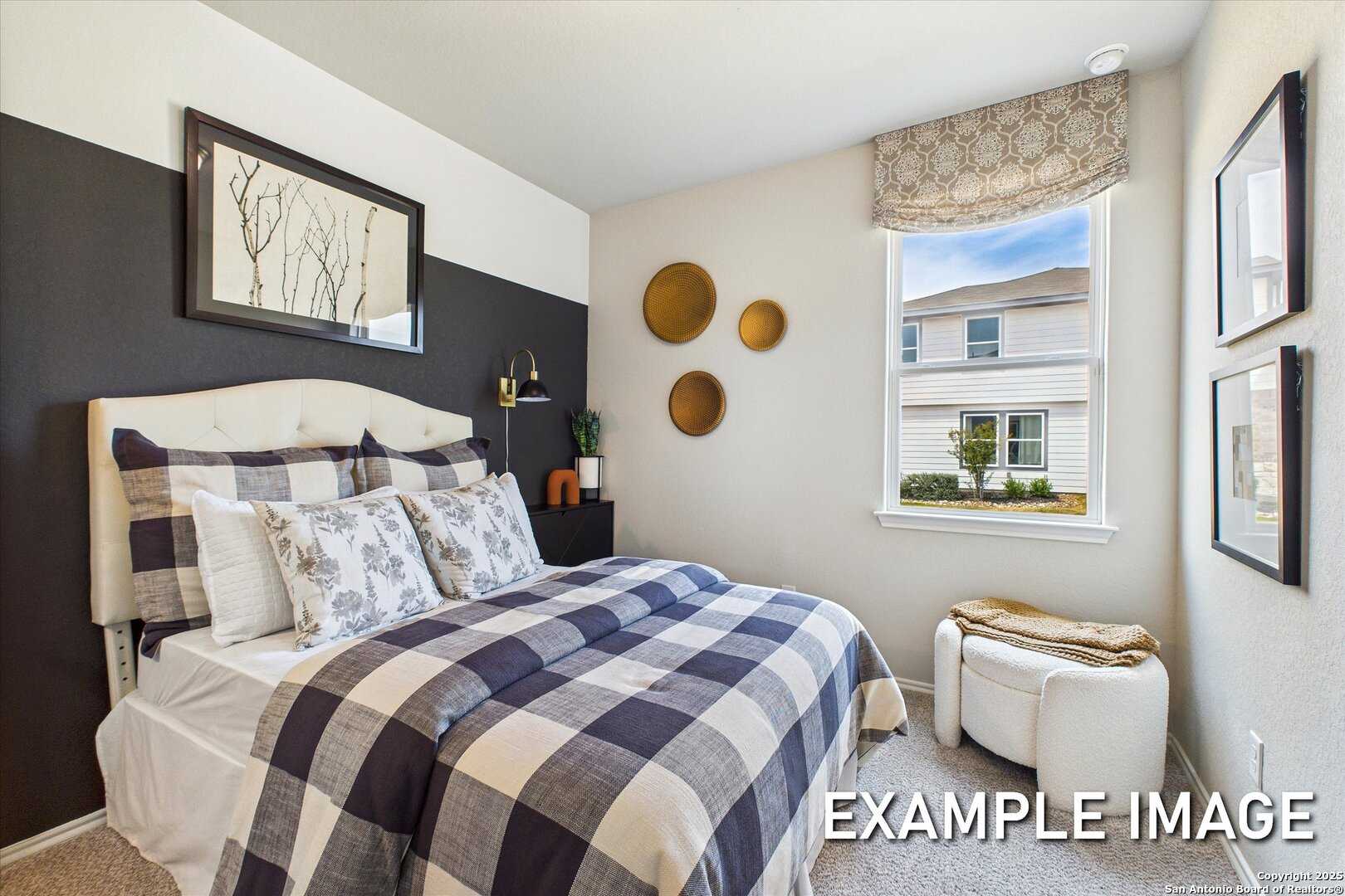 Cozy bedroom with checkered plaid bedding, wall art, potted plants, and suburban window view in Davidson Homes The Sabine C, San Antonio