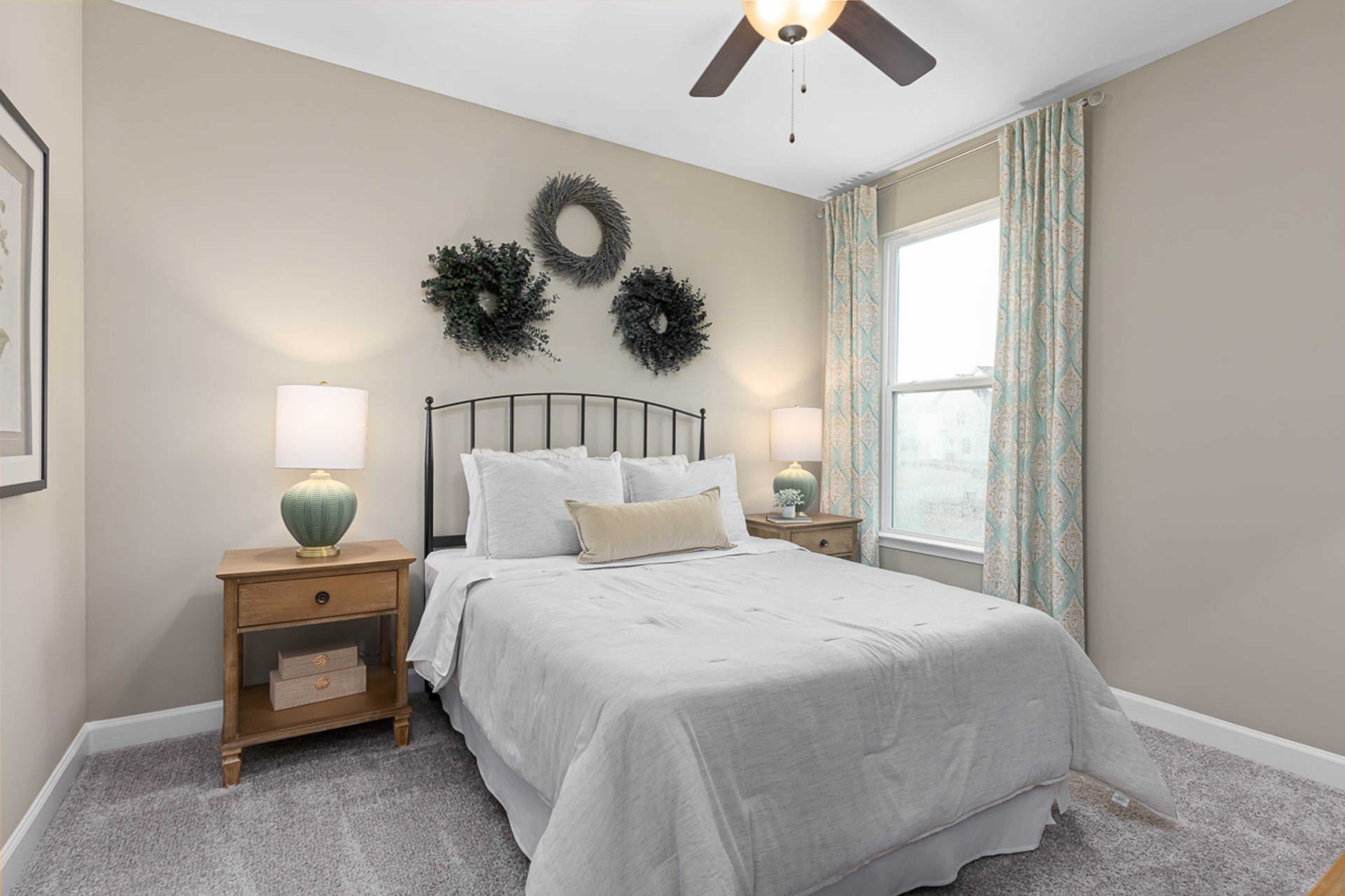Cozy bedroom at Weatherford East in Angier NC with queen bed, wooden nightstands, lamps, ceiling fan, and decorative wreaths by Davidson Homes