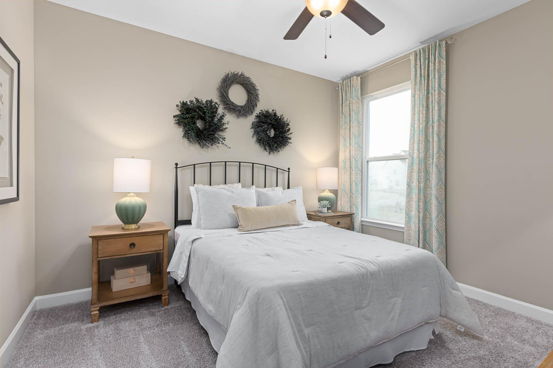 Cozy bedroom at Weatherford East in Angier NC with queen bed, wooden nightstands, lamps, ceiling fan, and decorative wreaths by Davidson Homes