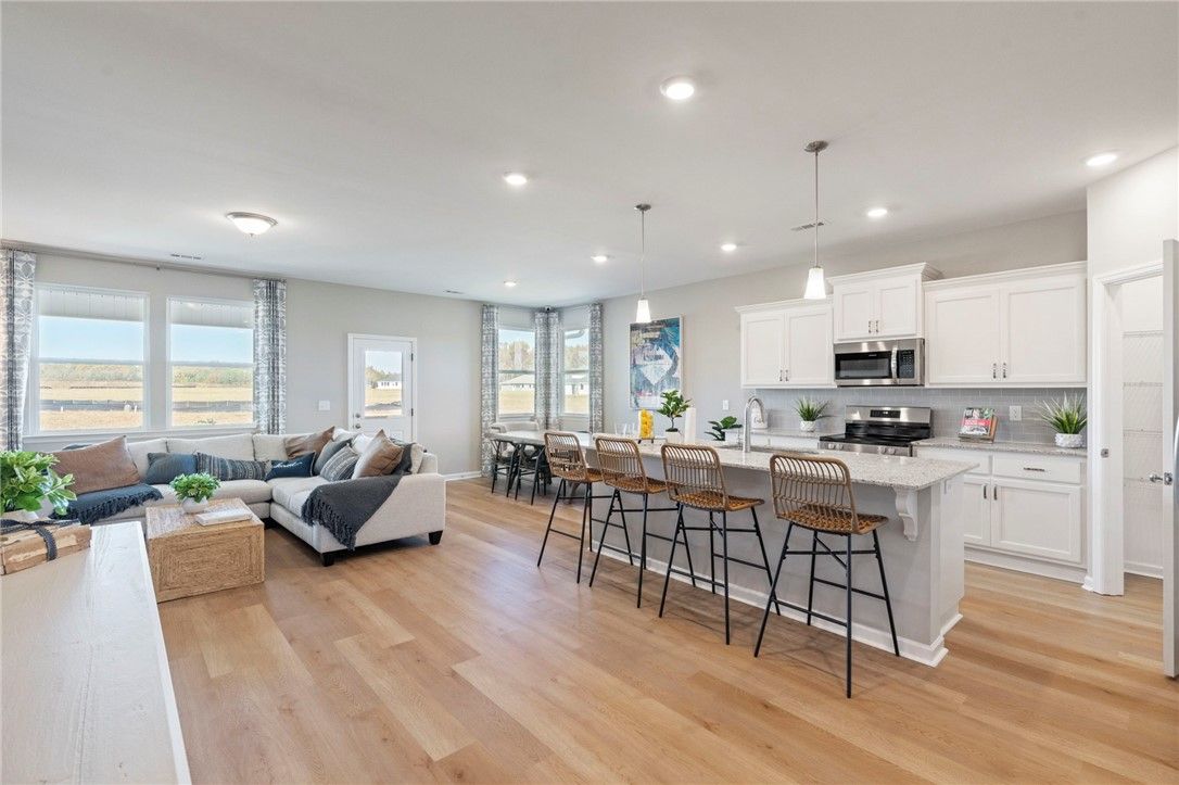Open-concept living room with L-shaped sofa and kitchen island, white cabinets, hardwood floors in Davidson Homes Phoenix B, Opelika