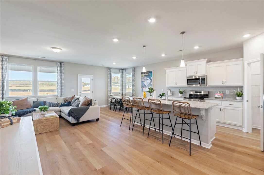 Open-concept living room with L-shaped sofa and kitchen island, white cabinets, hardwood floors in Davidson Homes Phoenix B, Opelika