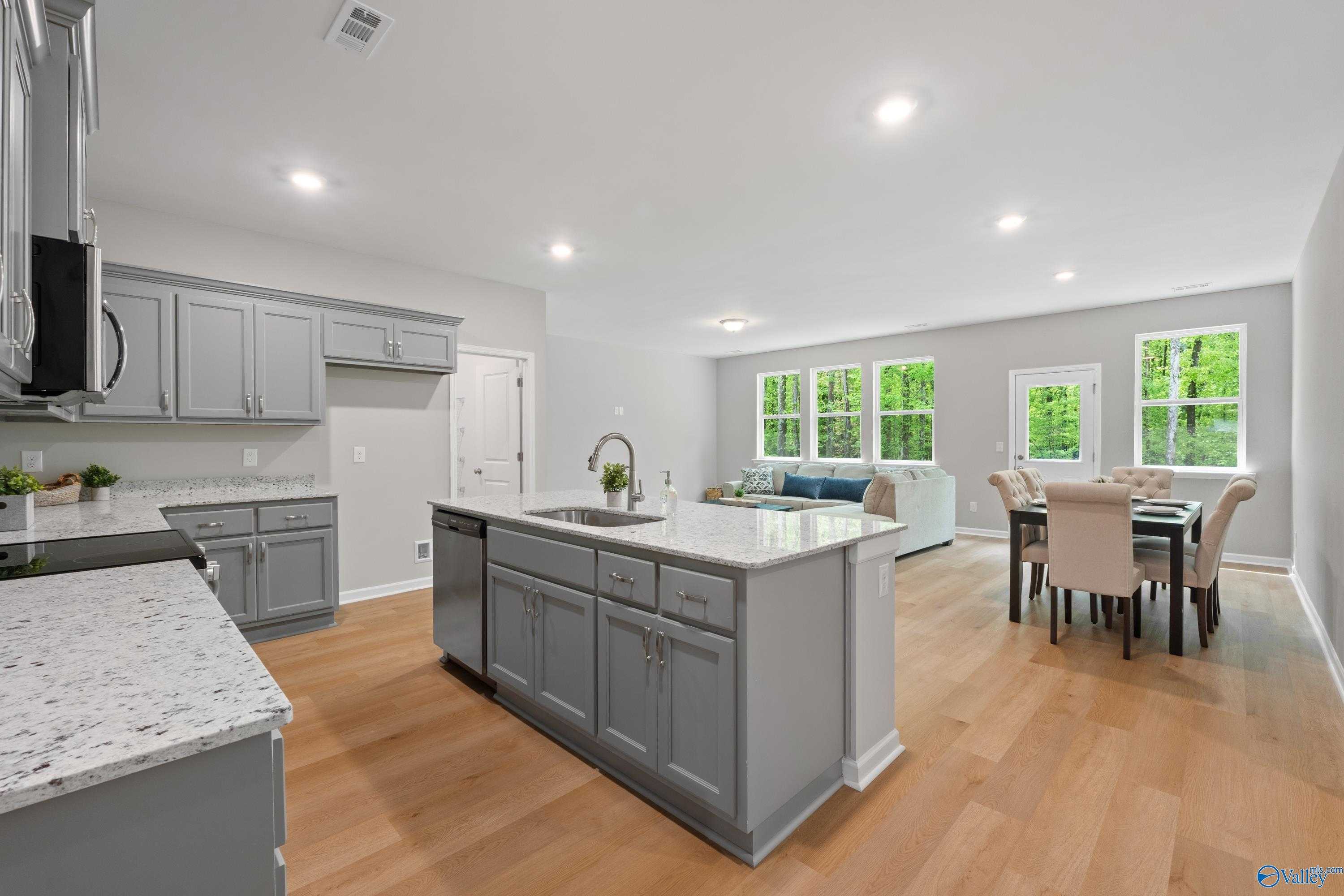 Open-concept kitchen with gray cabinets, white quartz island, and hardwood floors in The Luna 4-bedroom home, Hazel Green, Alabama