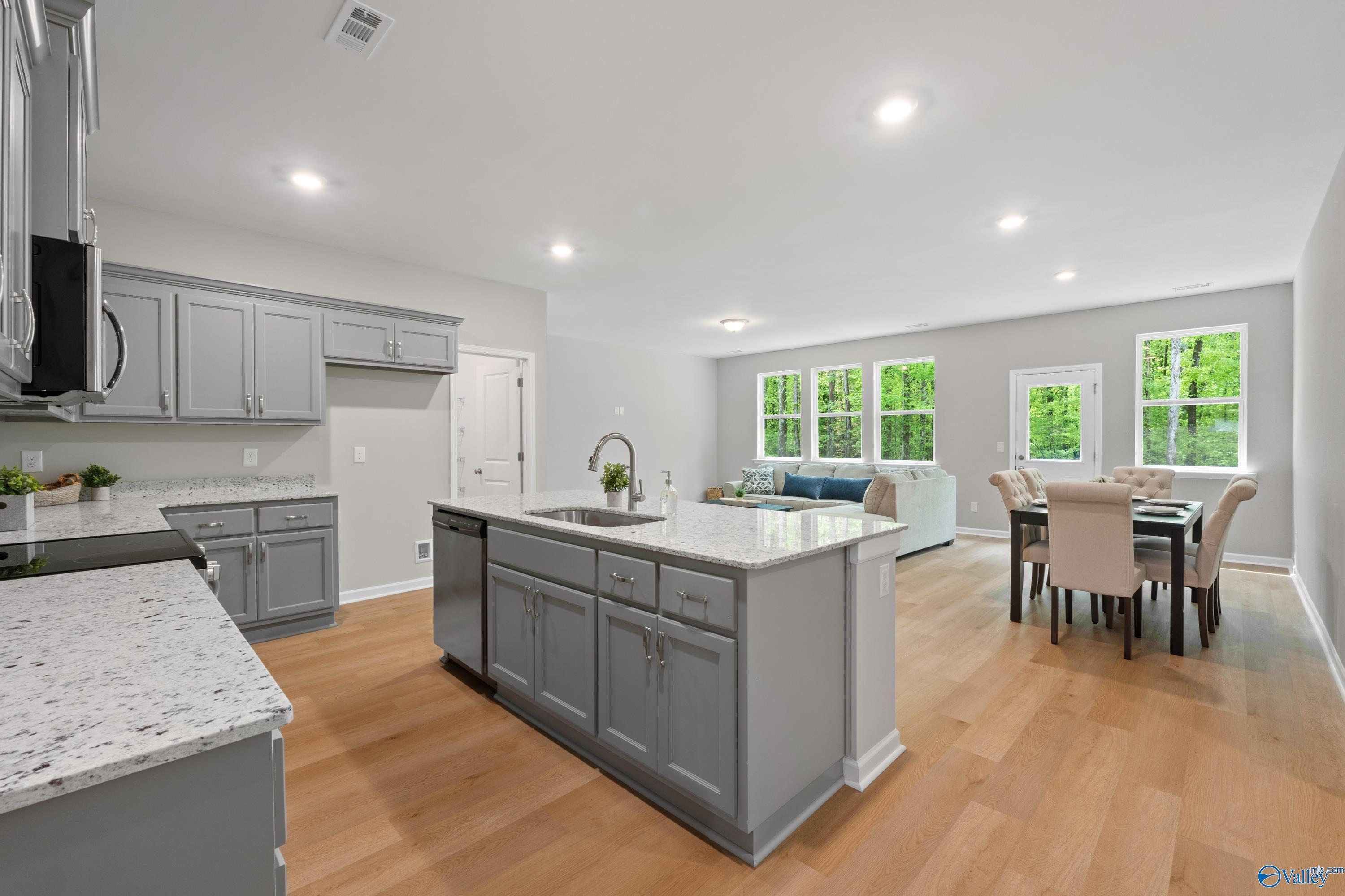 Open-concept kitchen with gray cabinets, white quartz island sink, and living-dining area in Davidson Homes The Luna, Hazel Green, Alabama