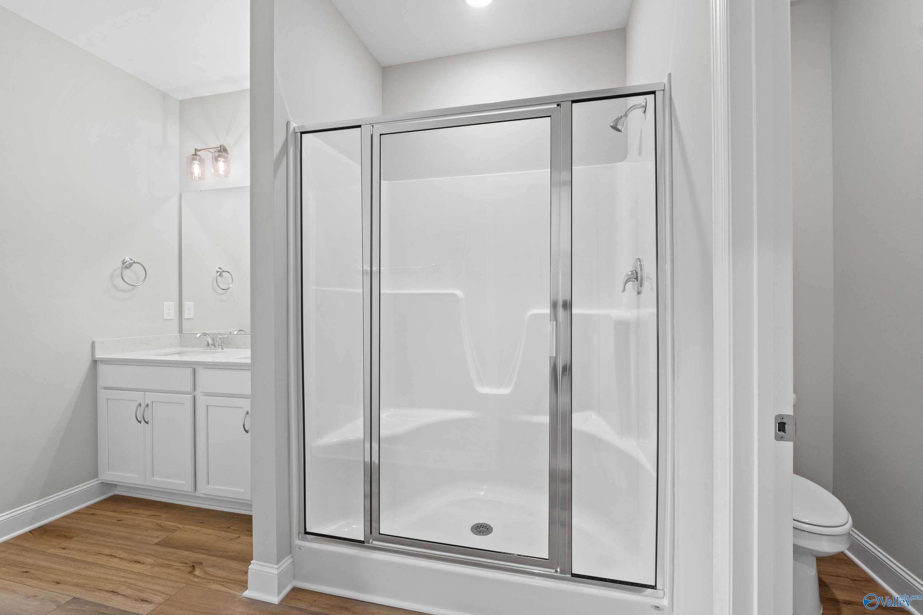 Modern white glass shower enclosure with tiled surround and double vanity in Davidson Homes bathroom, Athens Alabama