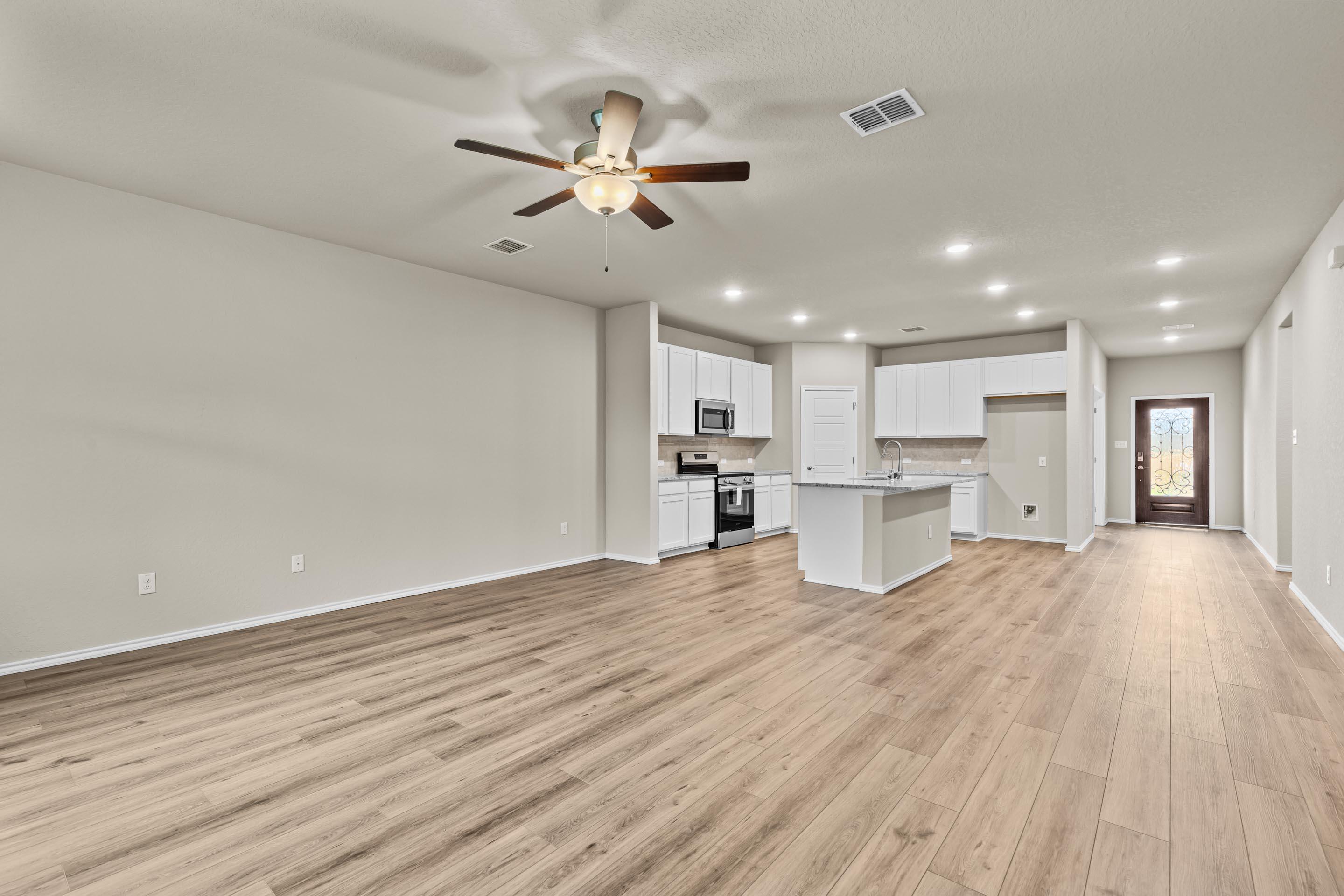 Modern open kitchen with white cabinets, stainless appliances, large island, and hardwood floors in Davidson Homes Douglas F, San Antonio