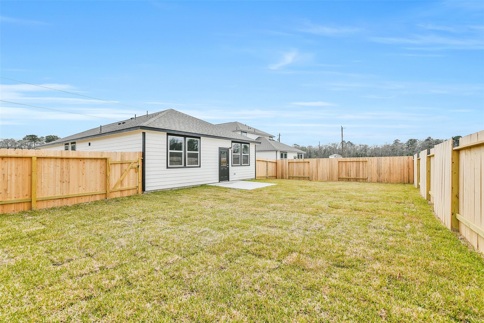 Rear view of single-story Davidson Homes The Frio G with fenced grassy backyard and patio in Liberty Estates, Cleveland, Texas
