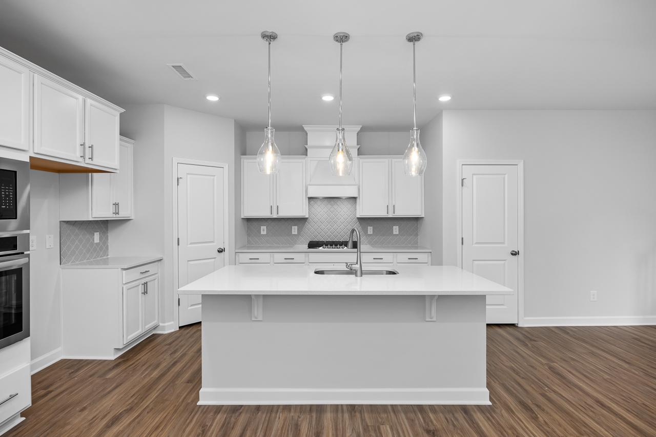 Spacious white kitchen in The Durham C with shaker cabinets, large island sink, three pendant lights, stainless appliances, hardwood floors