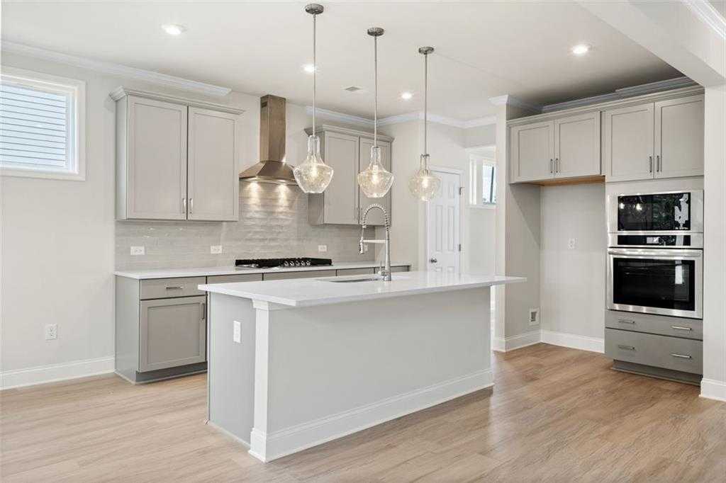 Modern kitchen featuring white quartz island, stainless double ovens, pendant lights in Davidson Homes The Willow D at Wehunt Meadows, Hoschton, GA