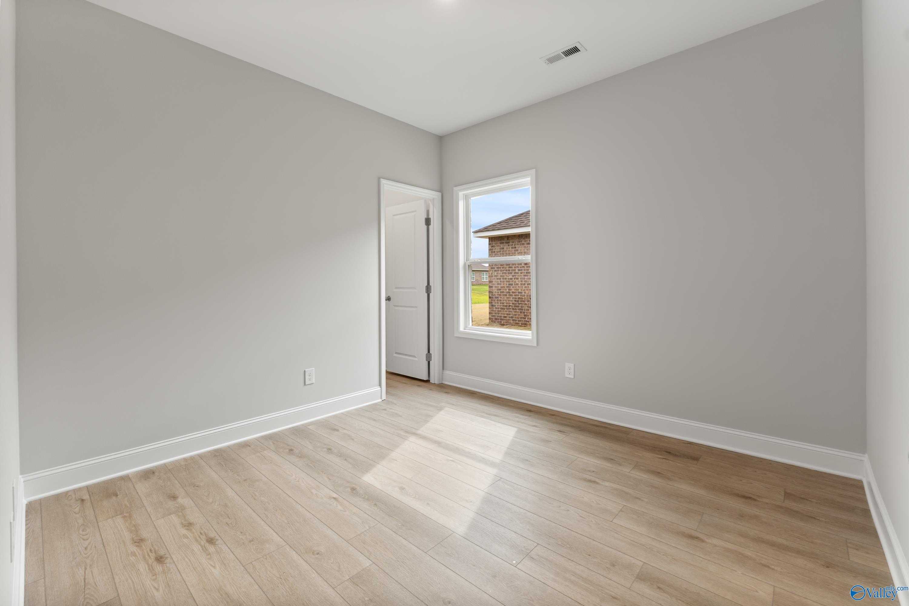 Sunny secondary bedroom with light gray walls, oak hardwood floors, and natural light in Davidson Homes The Daphne C, Athens, Alabama