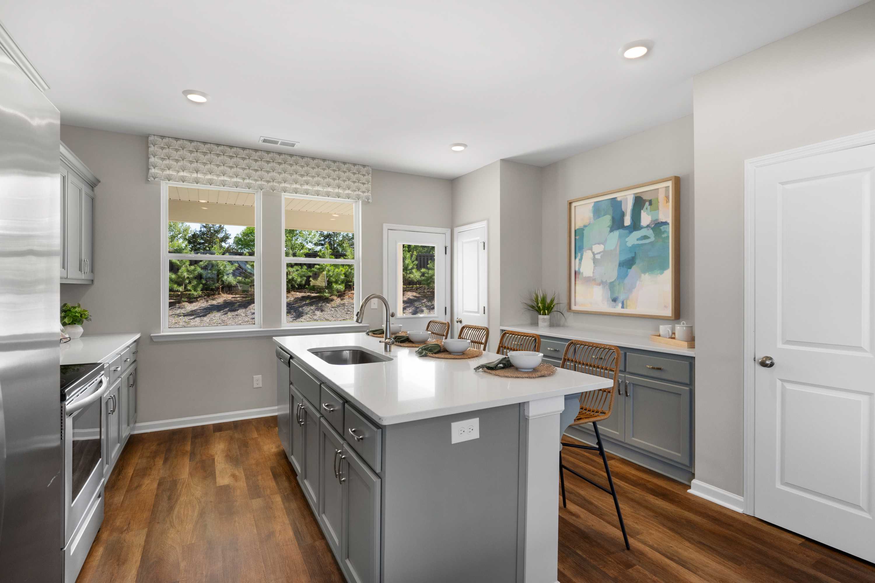 Modern kitchen in Evergreen Mill, Madison AL with white cabinets, gray island, stainless appliances, hardwood floors, large windows