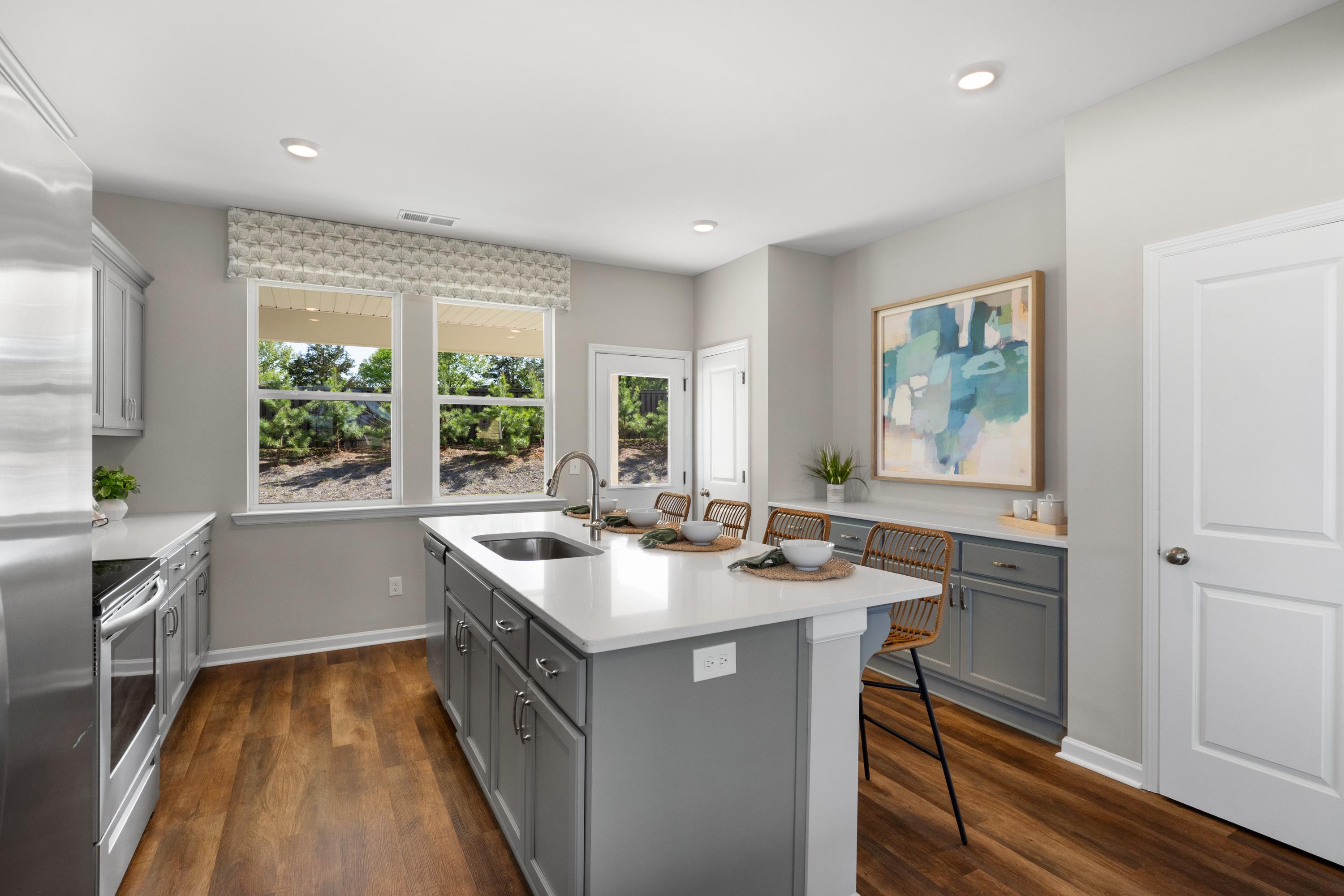 Modern kitchen in Evergreen Mill, Madison AL with white cabinets, gray island, stainless appliances, hardwood floors, large windows