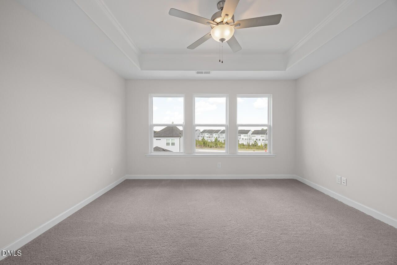 Spacious bedroom with tray ceiling, ceiling fan, carpet flooring, and triple windows in Davidson Homes The Mitchell plan, Knightdale NC