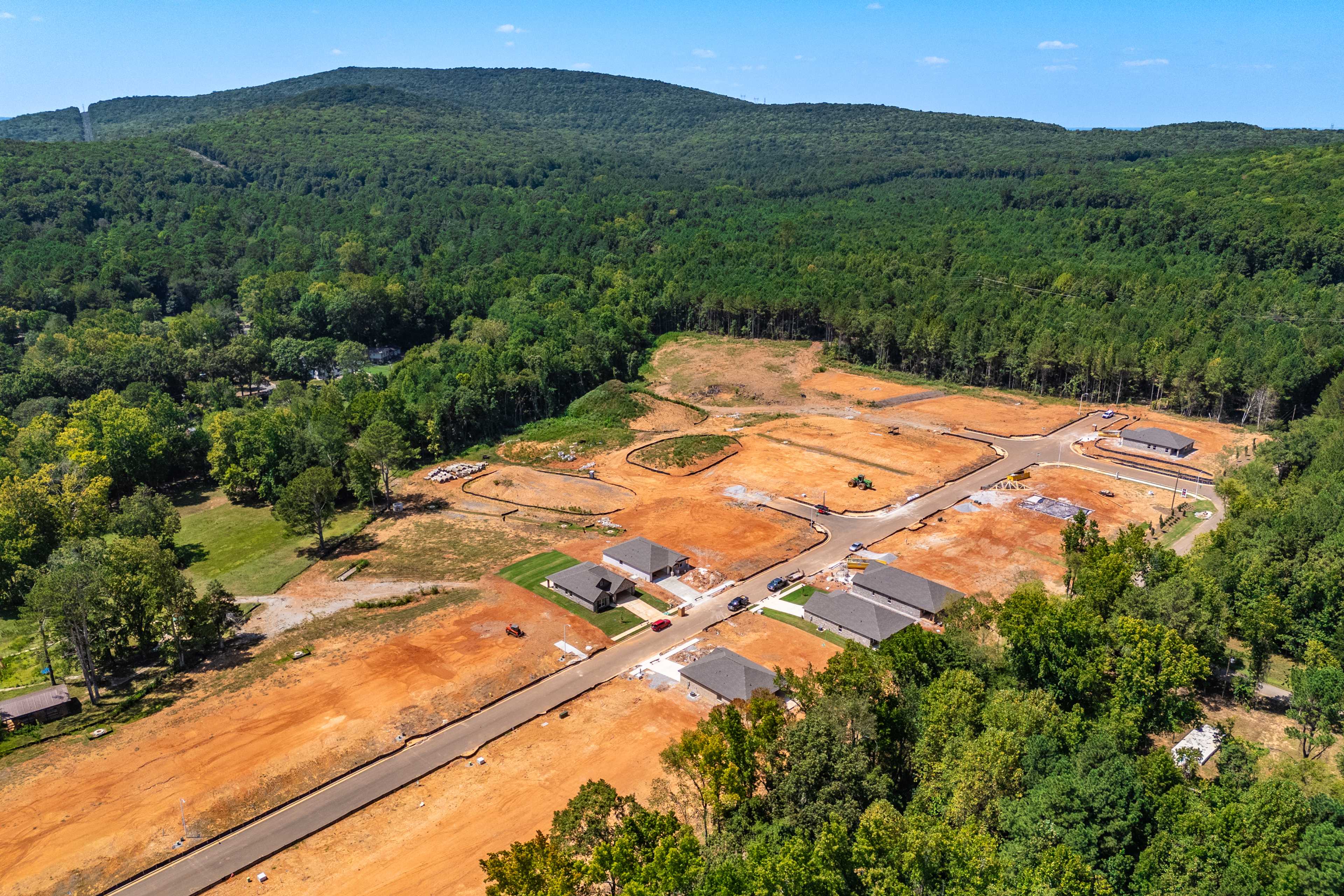 Aerial view of Spragins Cove neighborhood construction in Huntsville Alabama featuring new homes, dirt roads amid lush forests and mountain backdrop