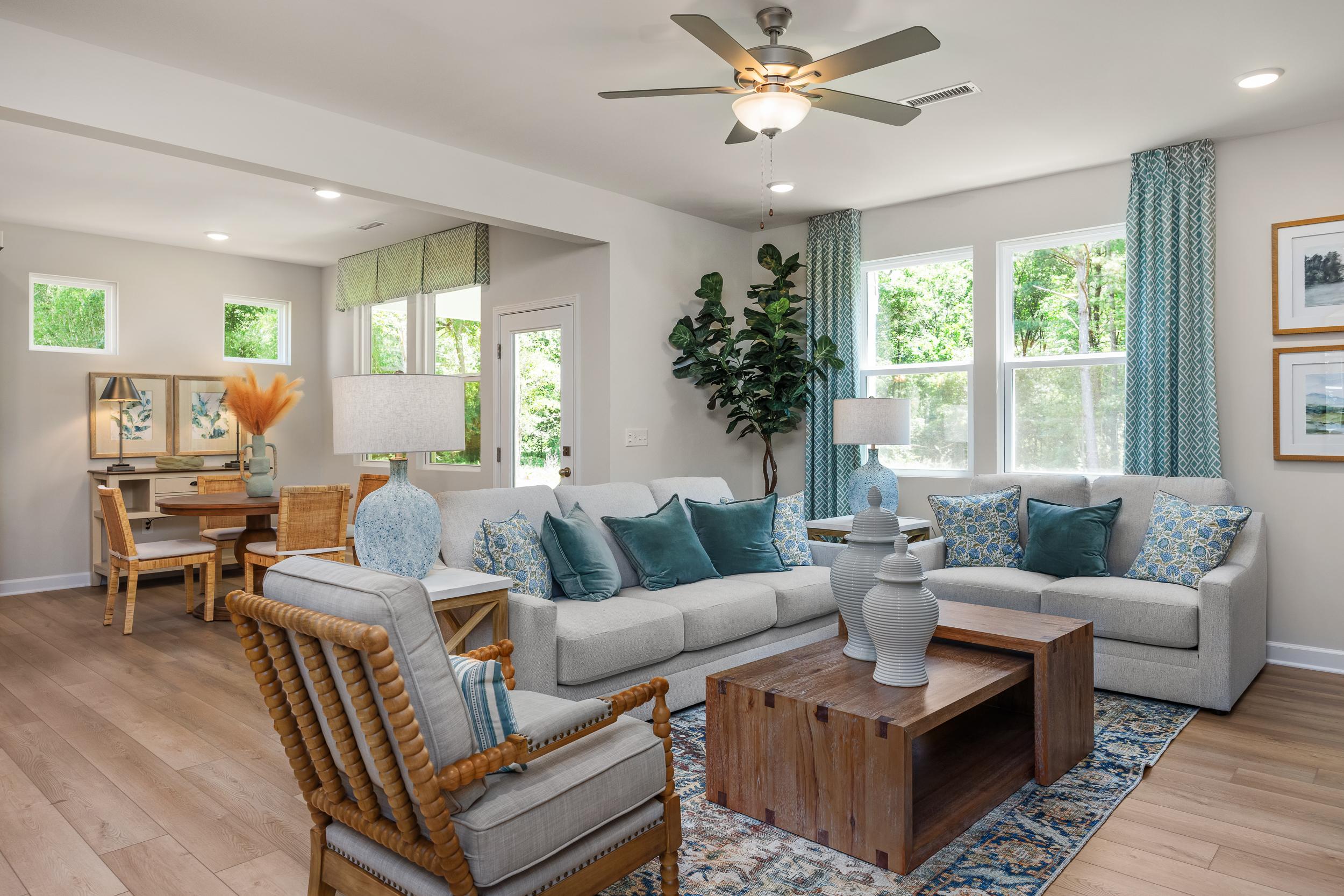 Open-concept living room at Retreat at North Main in Lillington NC featuring hardwood floors, ceiling fan, plush sofas, and large windows with plants