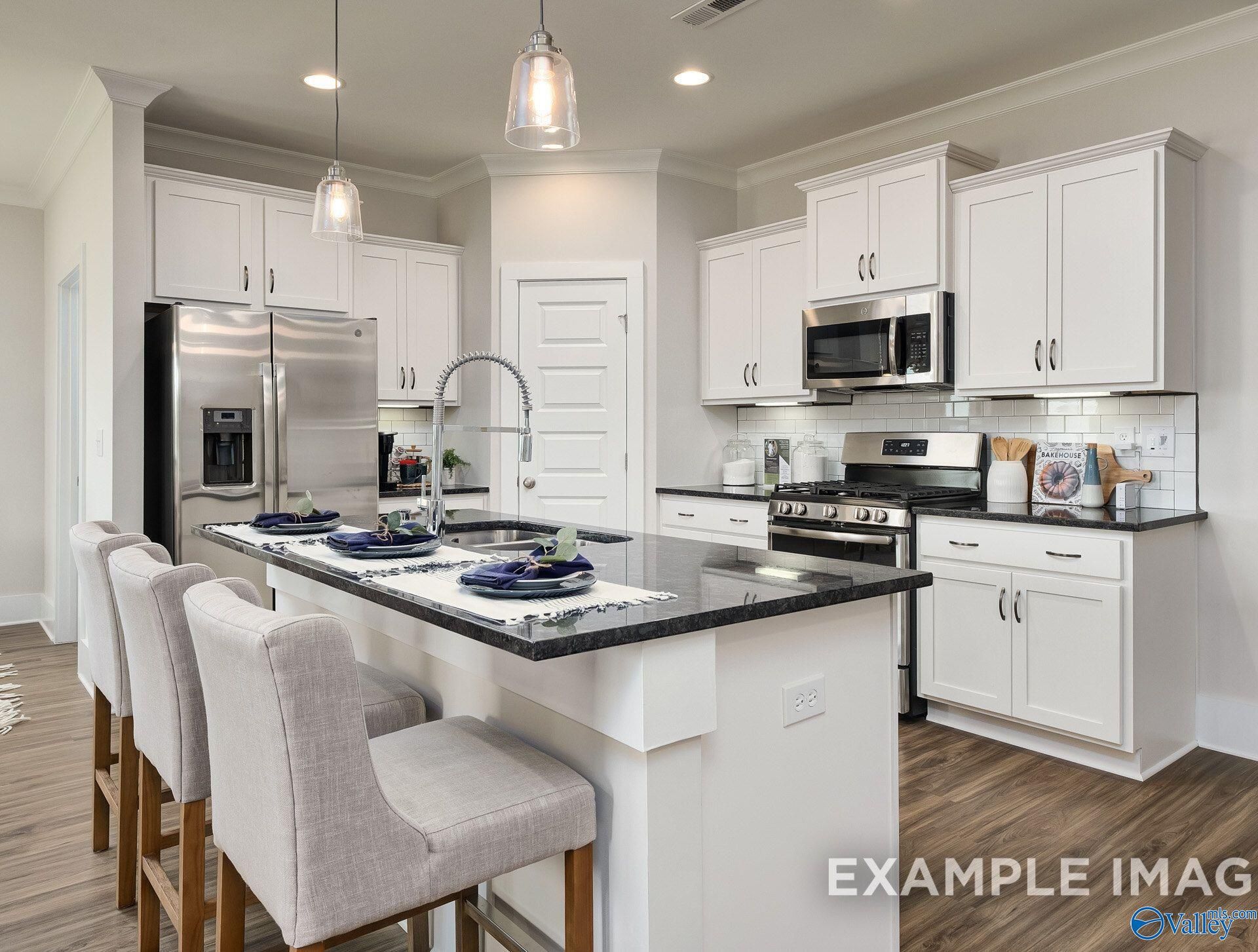 White kitchen island with granite countertops, bar seating, and stainless appliances in The Daphne D by Davidson Homes, Toney, Alabama