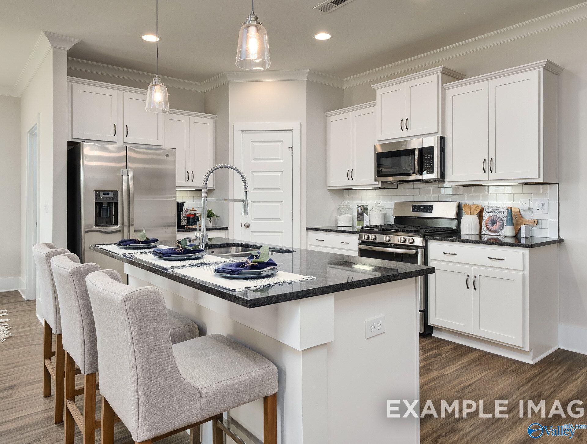 Kitchen island with dark granite countertops, white shaker cabinets, and stainless appliances in The Daphne D by Davidson Homes, Toney, Alabama
