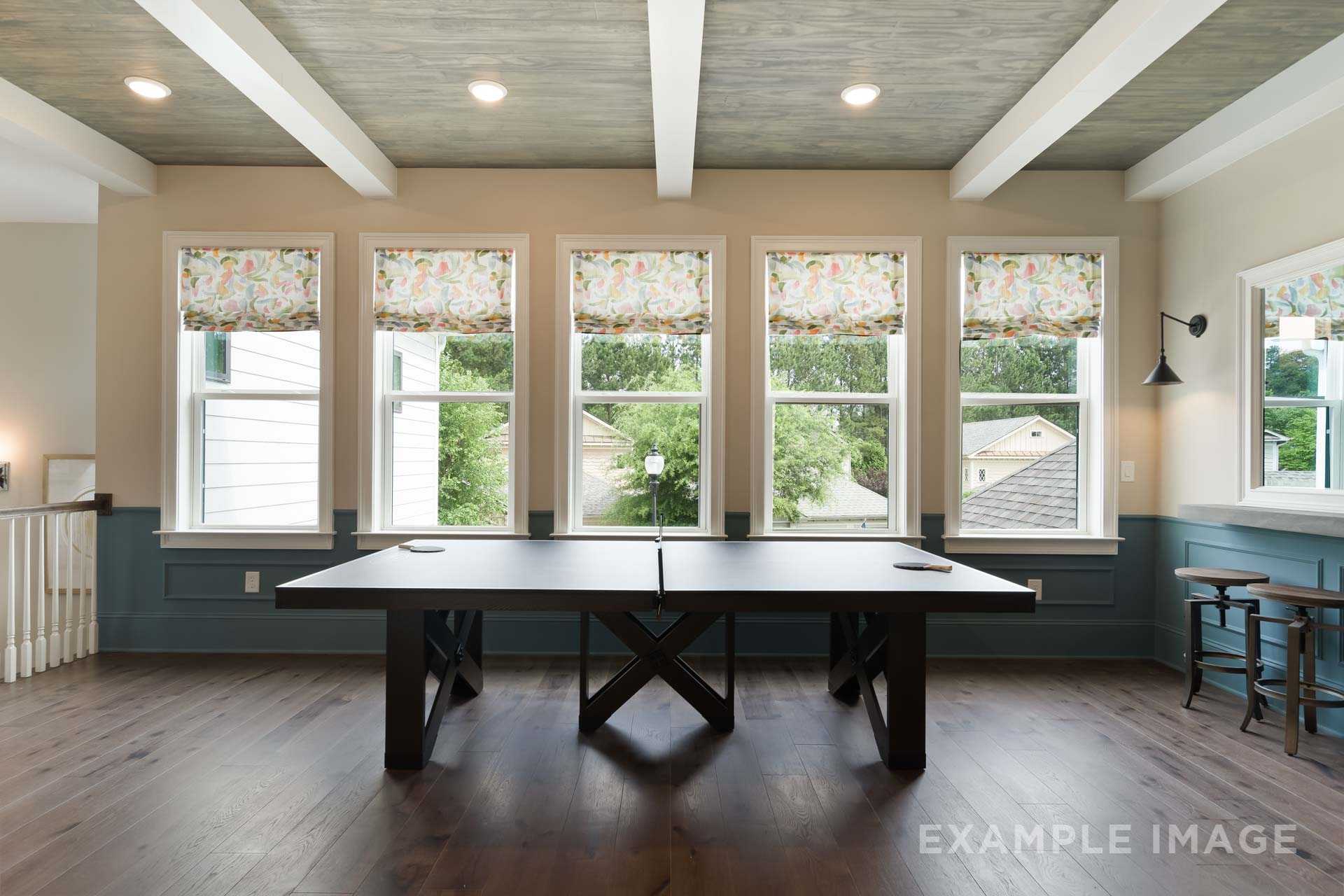Game room in The Seaside home design featuring black ping pong table, floral-curtained windows, and hardwood floors, Davidson Homes Woodstock GA