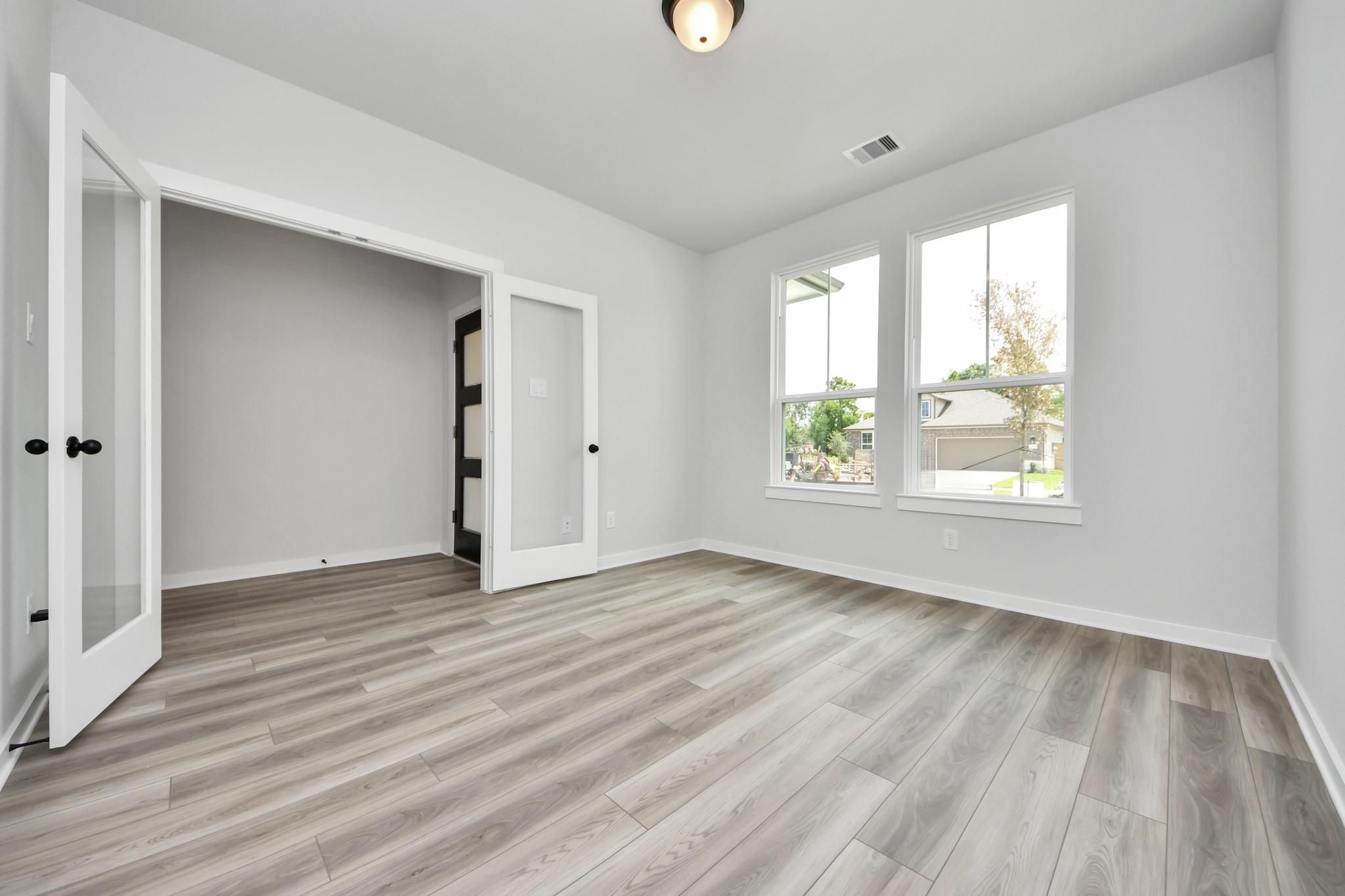 Bright home office or bedroom with French doors and wood-look flooring in The Sorrento E plan, Sundance Cove, Crosby, TX.