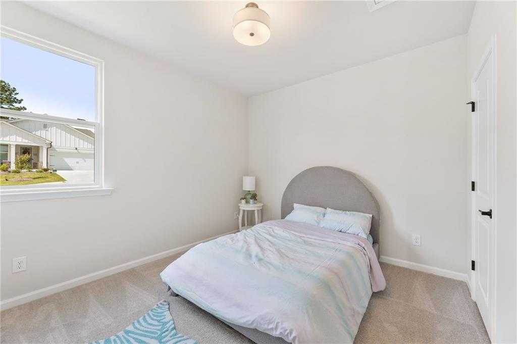 Cozy secondary bedroom with gray upholstered headboard bed, colorful striped bedding, bedside lamp, and large window in Davidson Homes The Daphne C, Loganville, GA
