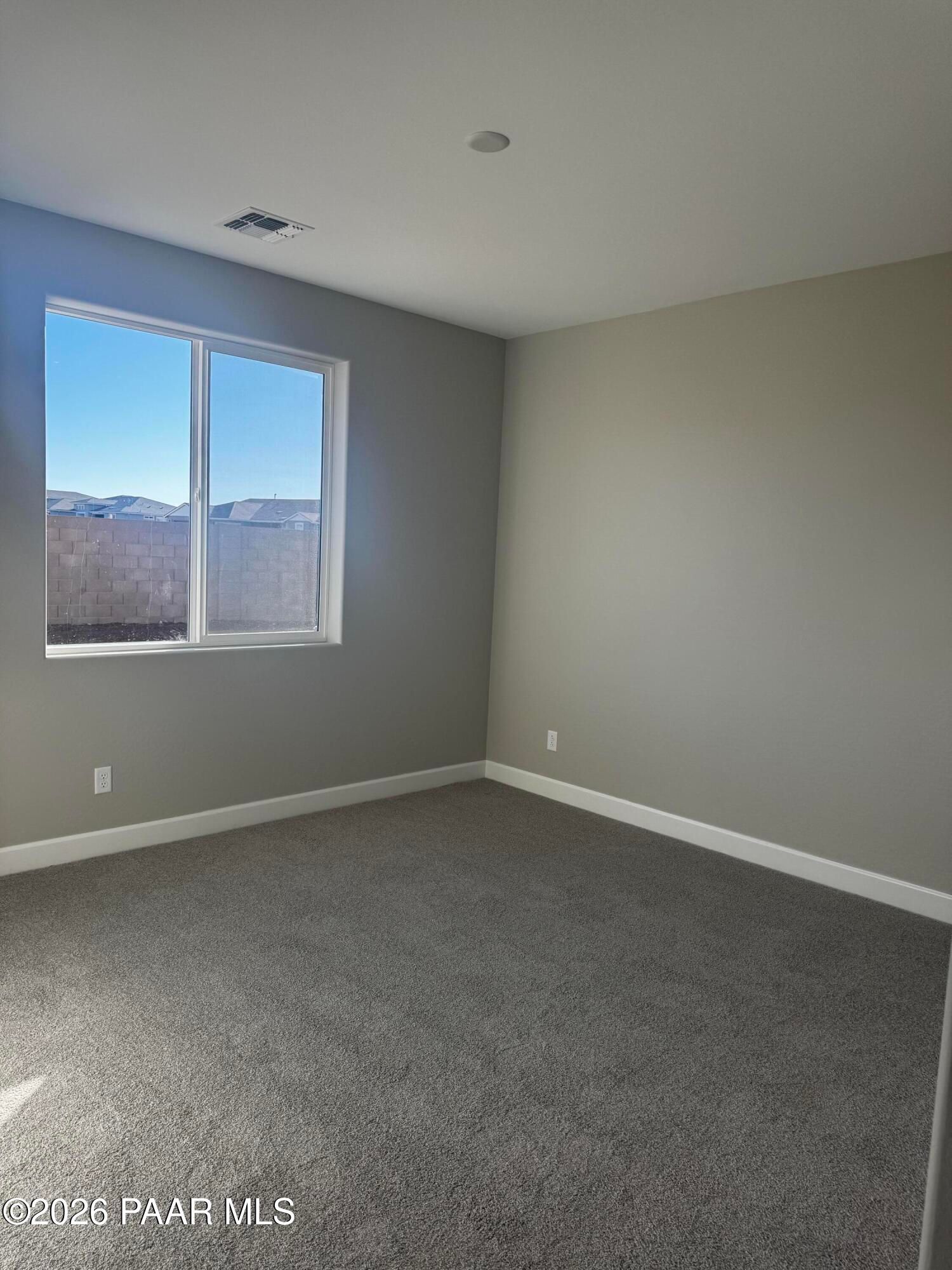 Bright bedroom with gray walls, beige carpet, and large window showing mountains in 3-bedroom Evermore Homes The Monarch B, Prescott Valley, Arizona