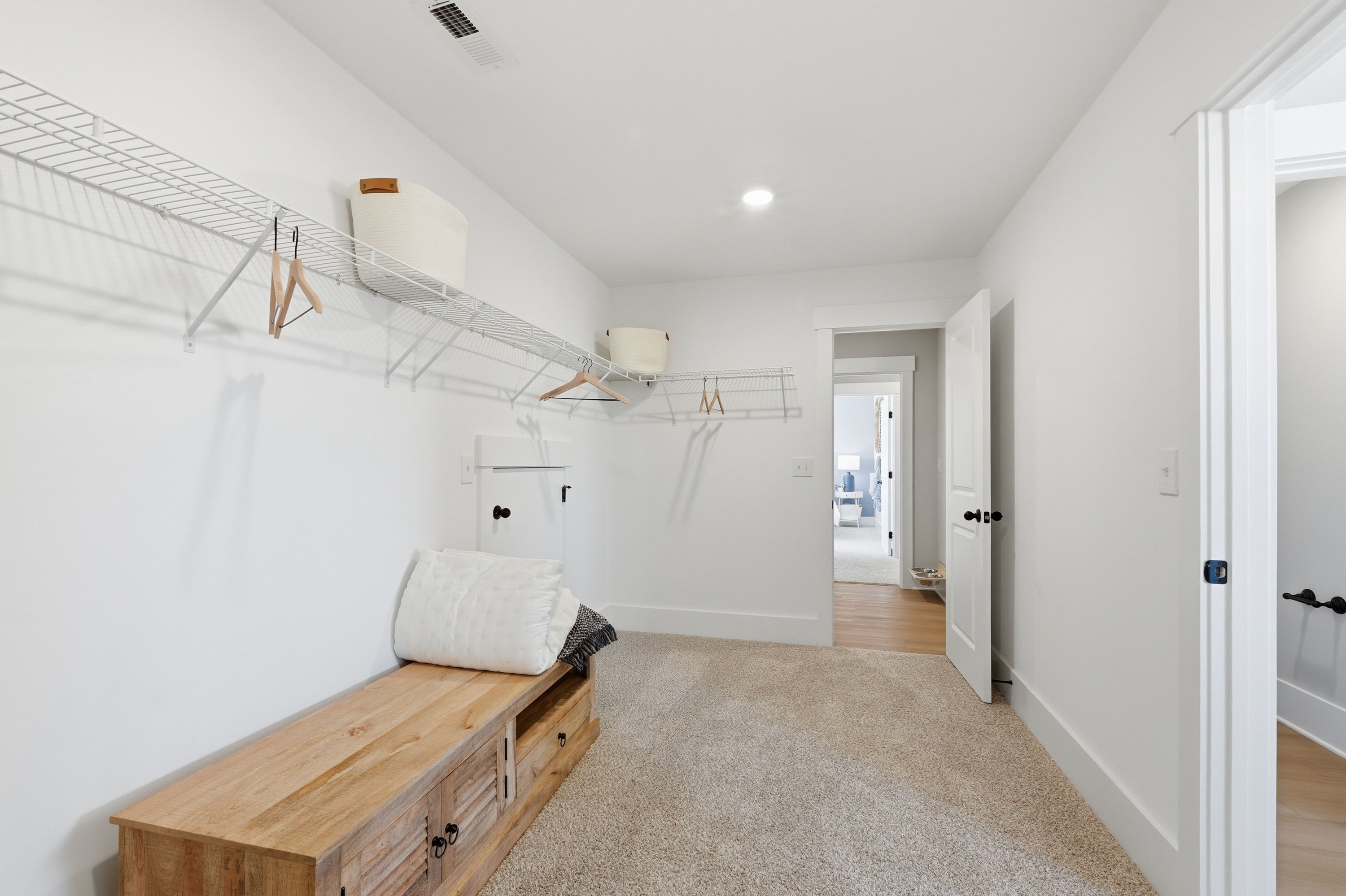 Spacious walk-in closet in Berry Cove home, New Market Alabama by Davidson Homes featuring wire shelving, wooden bench, and carpeted floor