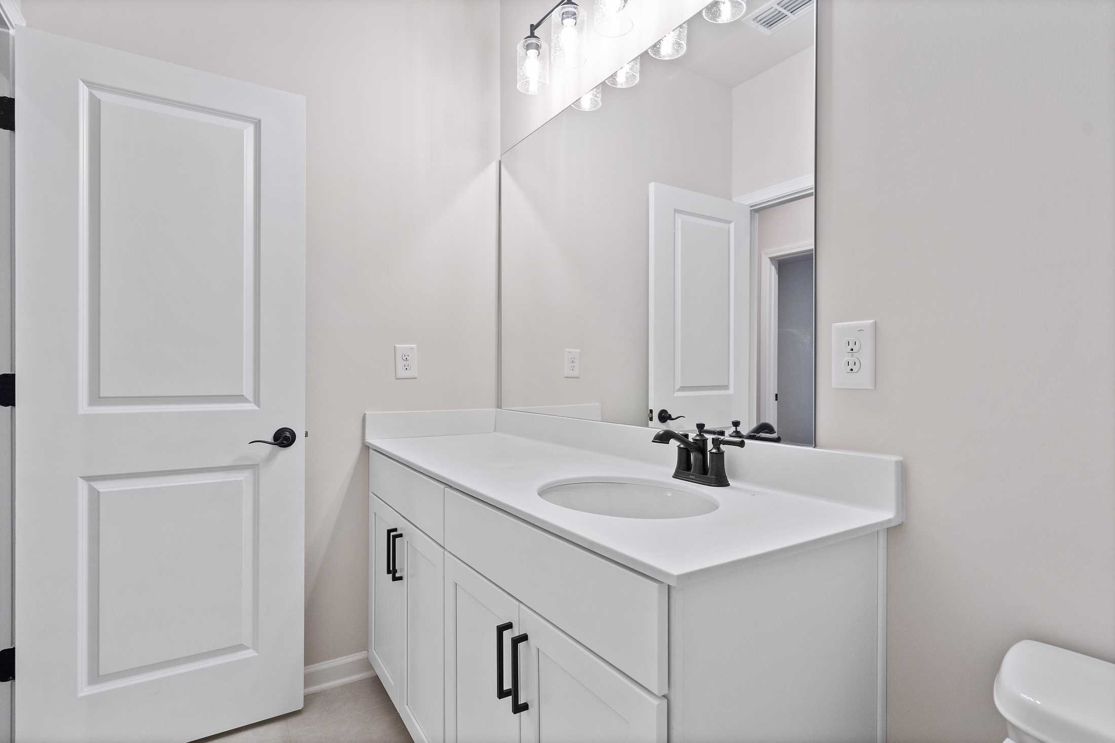 Modern master bathroom in The Glenwood B with white vanity, undermount sink, large mirror, and toilet by Davidson Homes Loganville GA