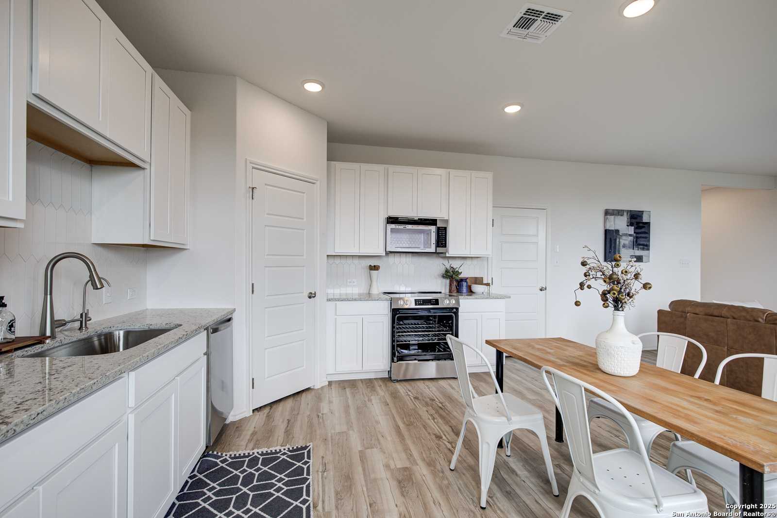 Modern white kitchen with granite counters, stainless appliances, open dining area in Davidson Homes Trinity A, San Antonio