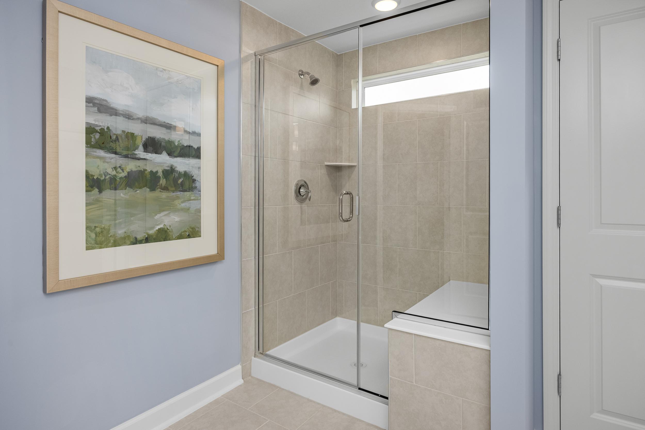 Spacious bathroom at Springvale in Fuquay-Varina NC with frameless glass shower, beige tiles, blue walls, and framed landscape art