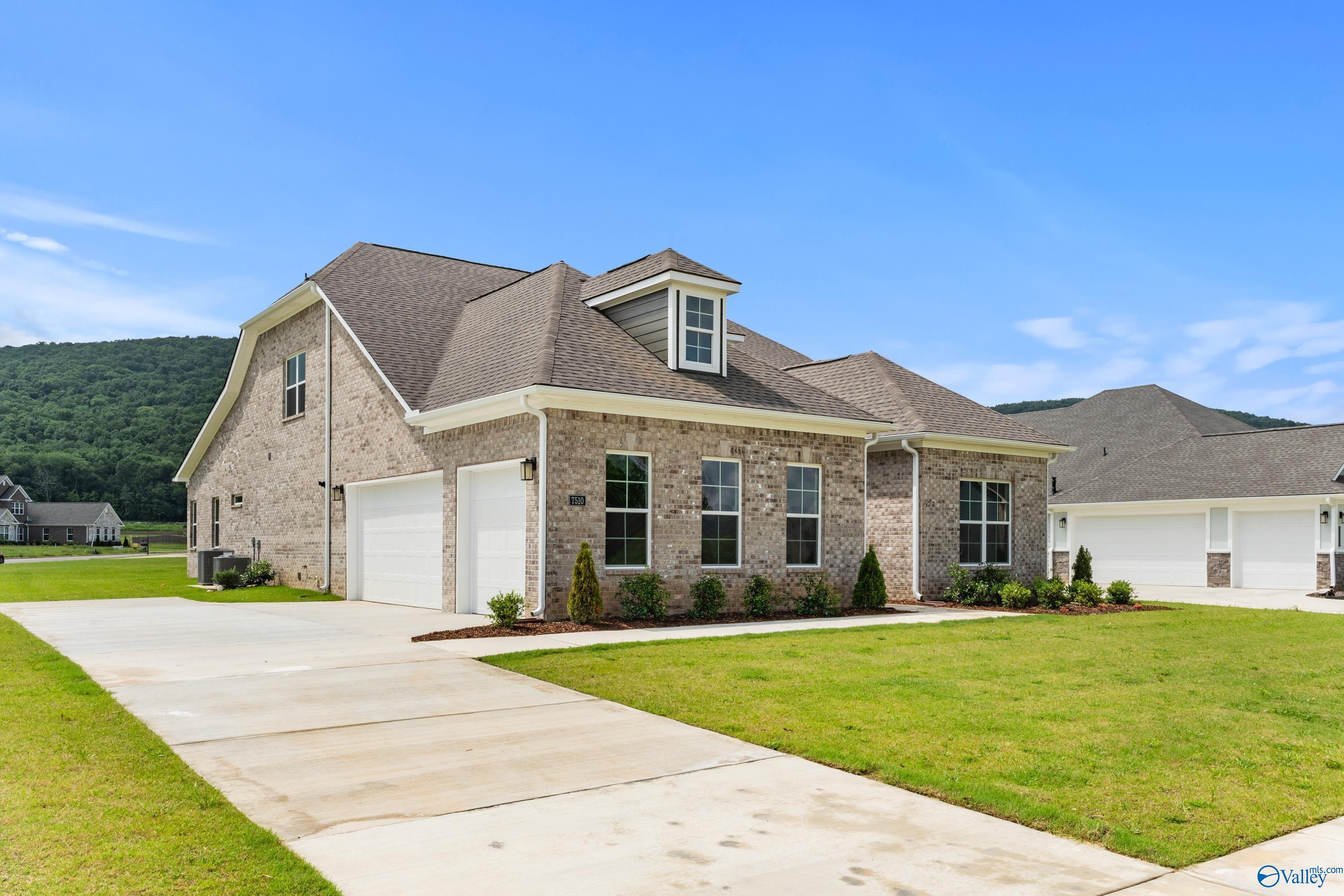 Brick 1.5-story home with dormer, garage, and landscaped yard in The Meadows at Hampton Cove, Owens Cross Roads, Alabama