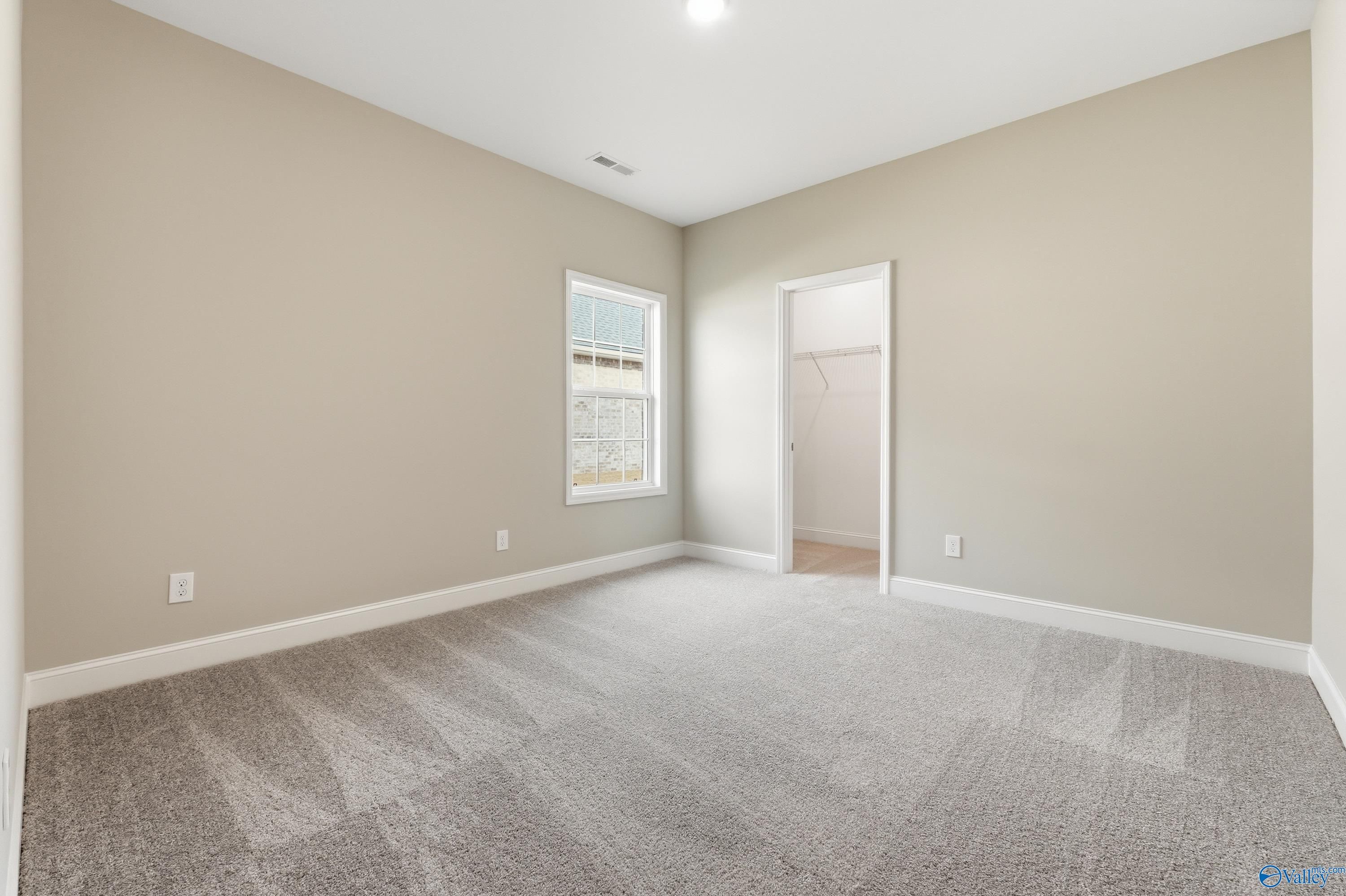 Bright secondary bedroom with beige walls, gray carpet, large window, and walk-in closet in Davidson Homes The Lanier, Meridianville, Alabama