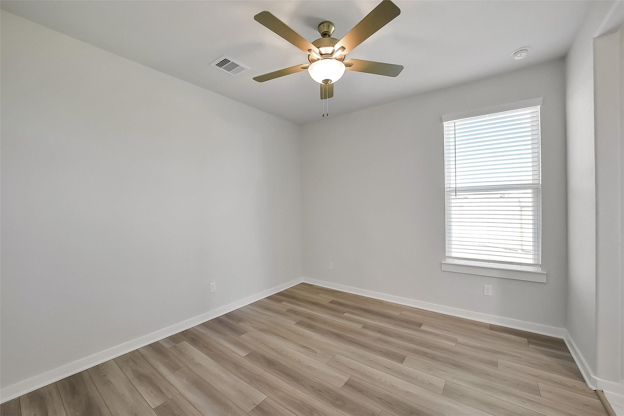 Bright bedroom with ceiling fan, luxury vinyl plank floors, and window blinds in Davidson Homes Acadia A, Sunterra, Katy, Texas