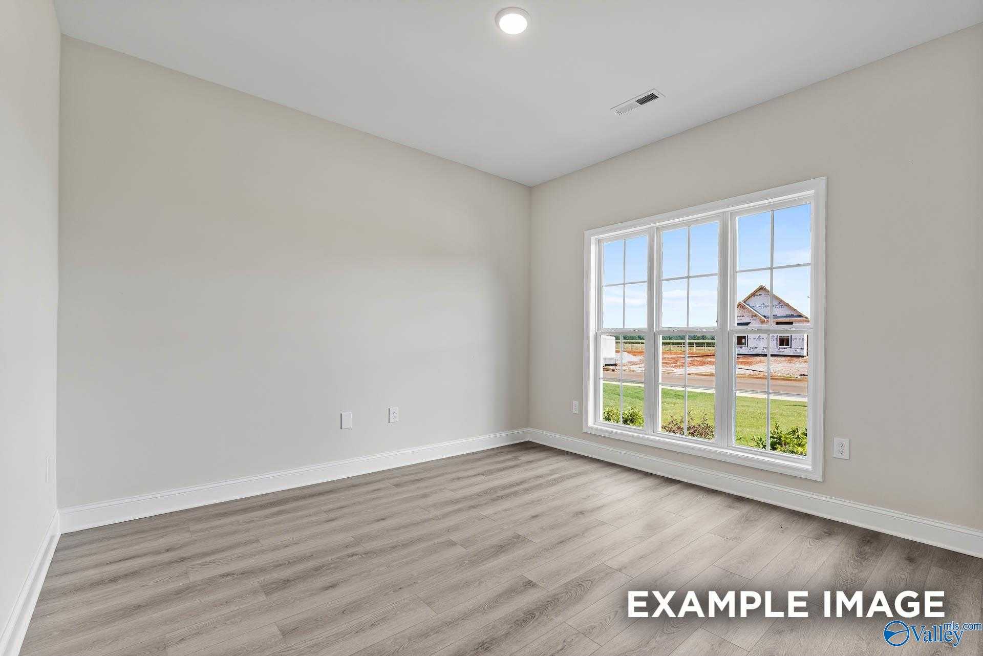 Bright secondary bedroom with neutral walls, laminate flooring, and window view of green field in Davidson Homes The Finleigh, Meridianville, Alabama